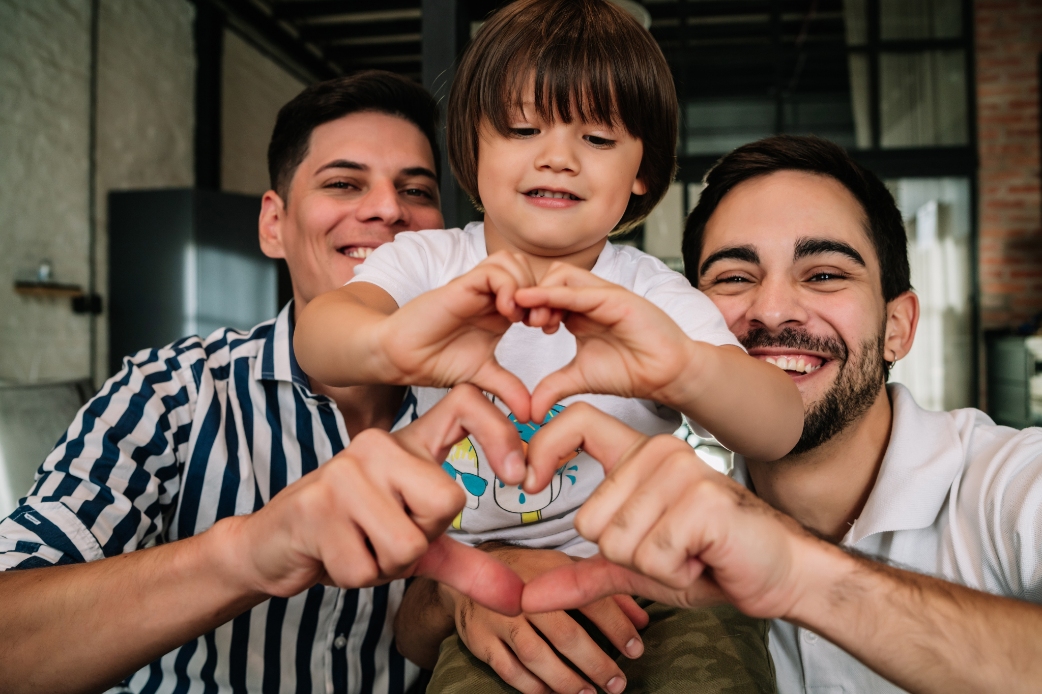 A joyful family moment featuring two fathers and their child forming heart shapes with their hands in Portland, Oregon, or Seattle, Washington, symbolizing the love, unity, and emotional security that define secure attachment.