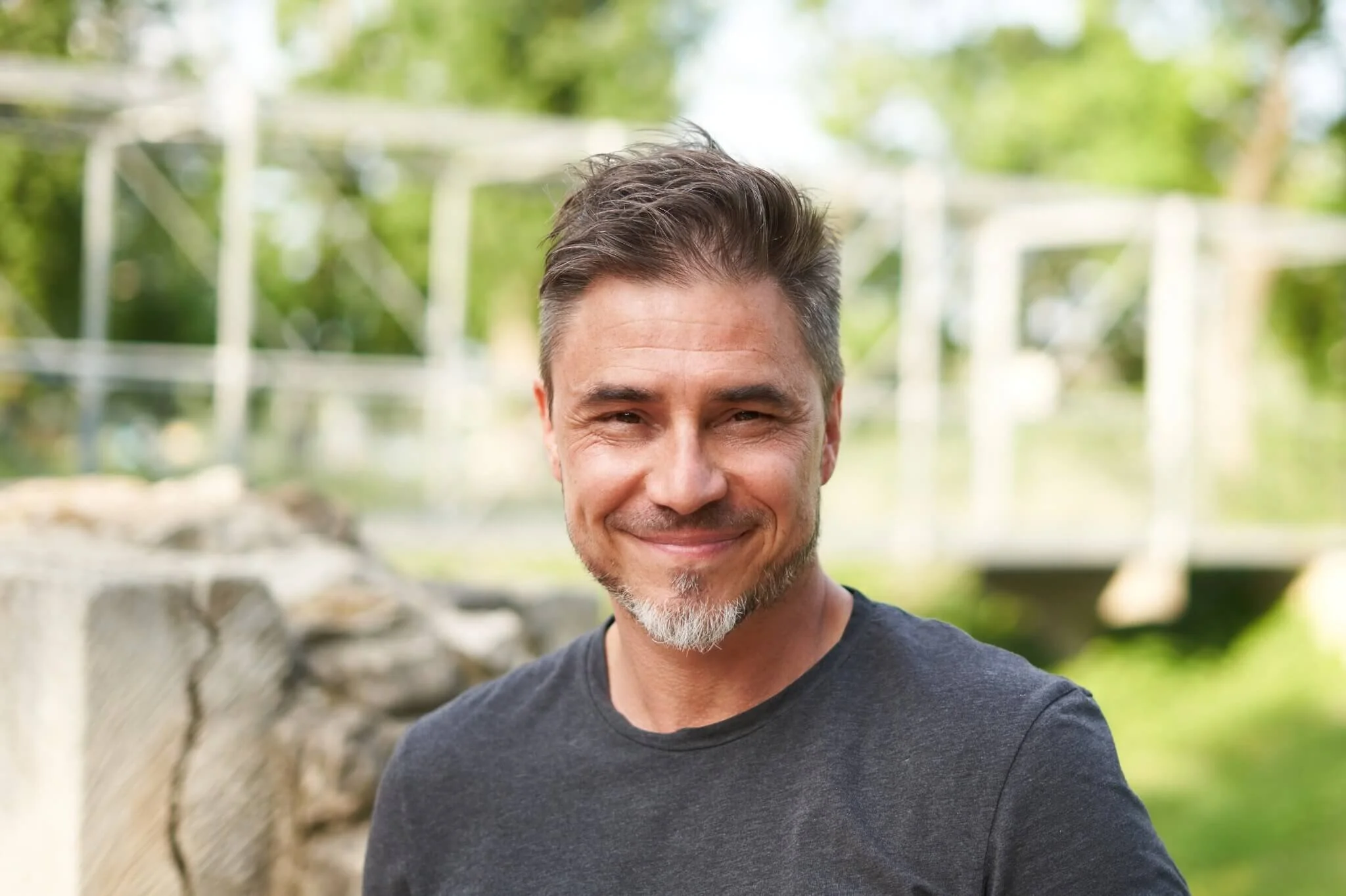A mature older man wearing a grey shirt & smiling outside near a bridge. Discover how workplace stress therapy in Seattle, WA can help with perfectionism, burnout & more. Get started today.