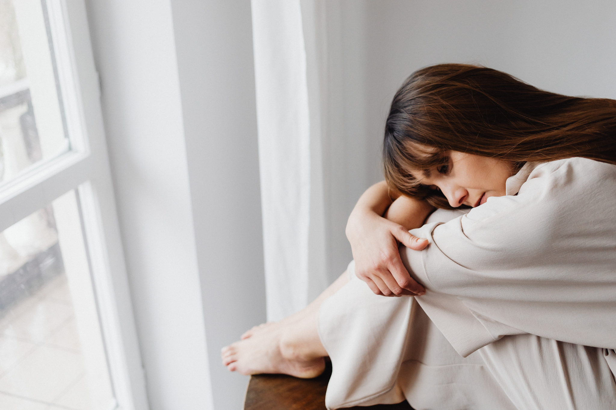 A woman sits thoughtfully by a bright window. Trust rebuilding after cheating requires guided compassion. affair recovery counseling in Lake Oswego, Oregon. We support your relationship's journey forward in the 97035 zip code.