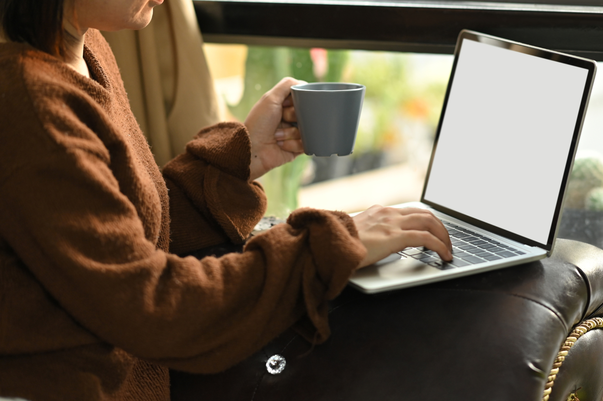 A woman wearing a sweater typing on a laptop & holding a mug. If you're experiencing distance in your relationship, a couples therapist in Portland, Or can help you. Learn more here!