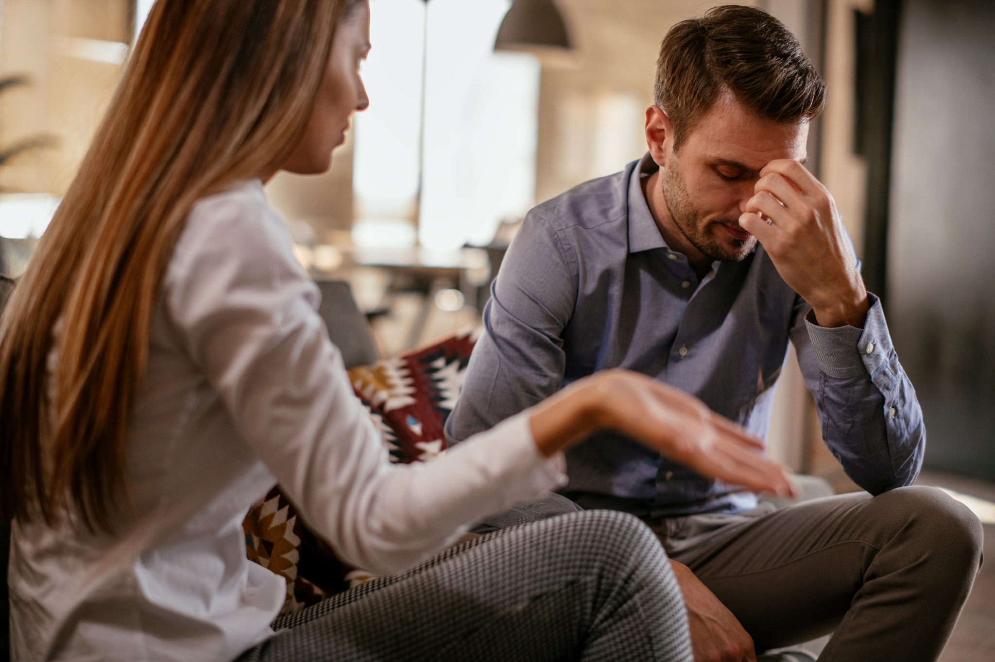 A woman gesturing while a man appears distressed during a serious conversation on a sofa. This indoor scene symbolizes the importance of communication, attachment styles, and couples counseling in Portland, Oregon, near zip codes 97214 and 97210.