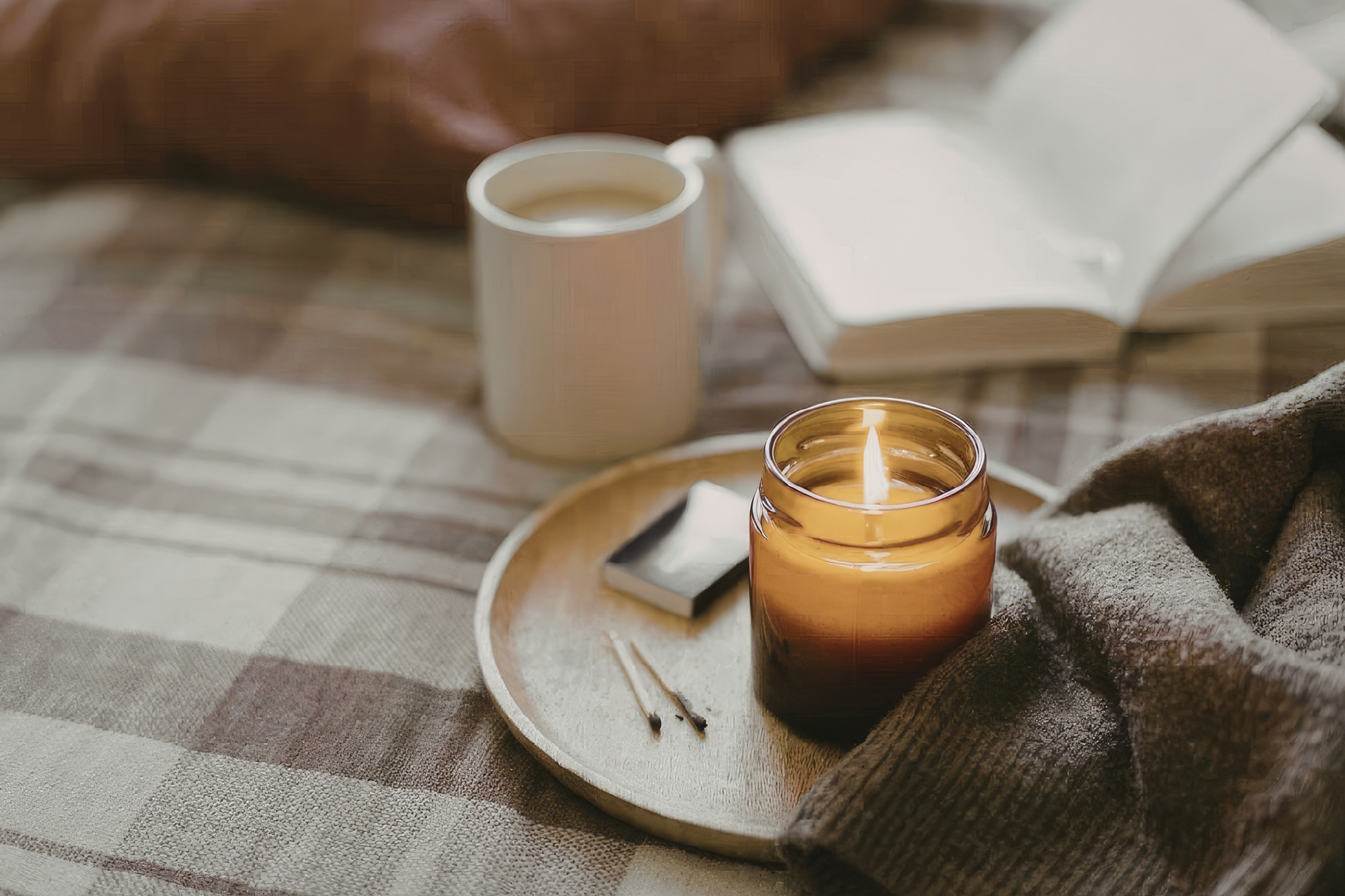A cozy indoor scene with a plaid blanket, a lit candle, a mug of tea, and an open book in Portland, Oregon, or Seattle, Washington, symbolizing the self-soothing practices often embraced by individuals with avoidant attachment styles.