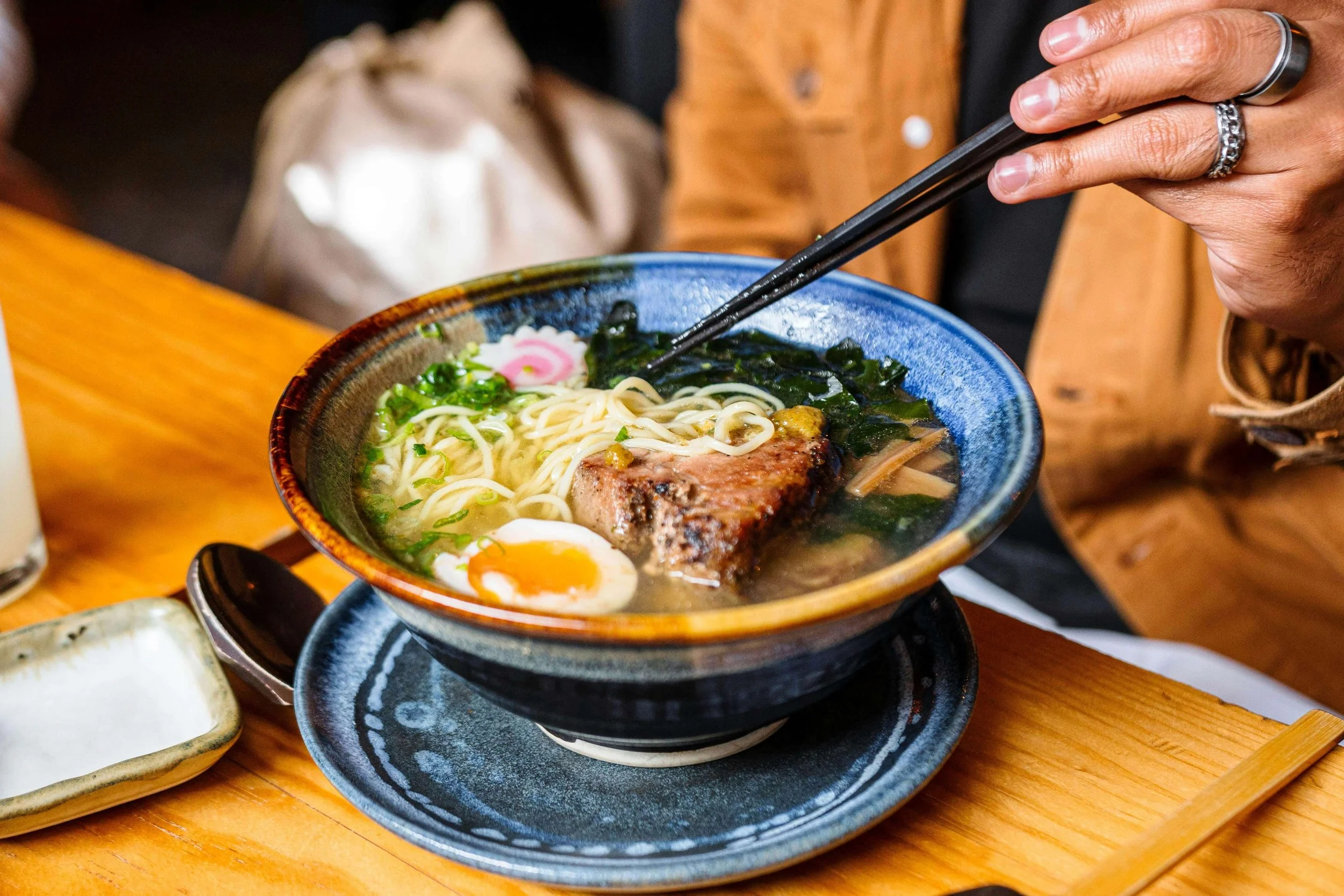A hand grabbing ramen in a handmade blue bowl. Read our blog for more date night ideas in Portland, OR. Start working with a couples counselor today to improve communication & connection.
