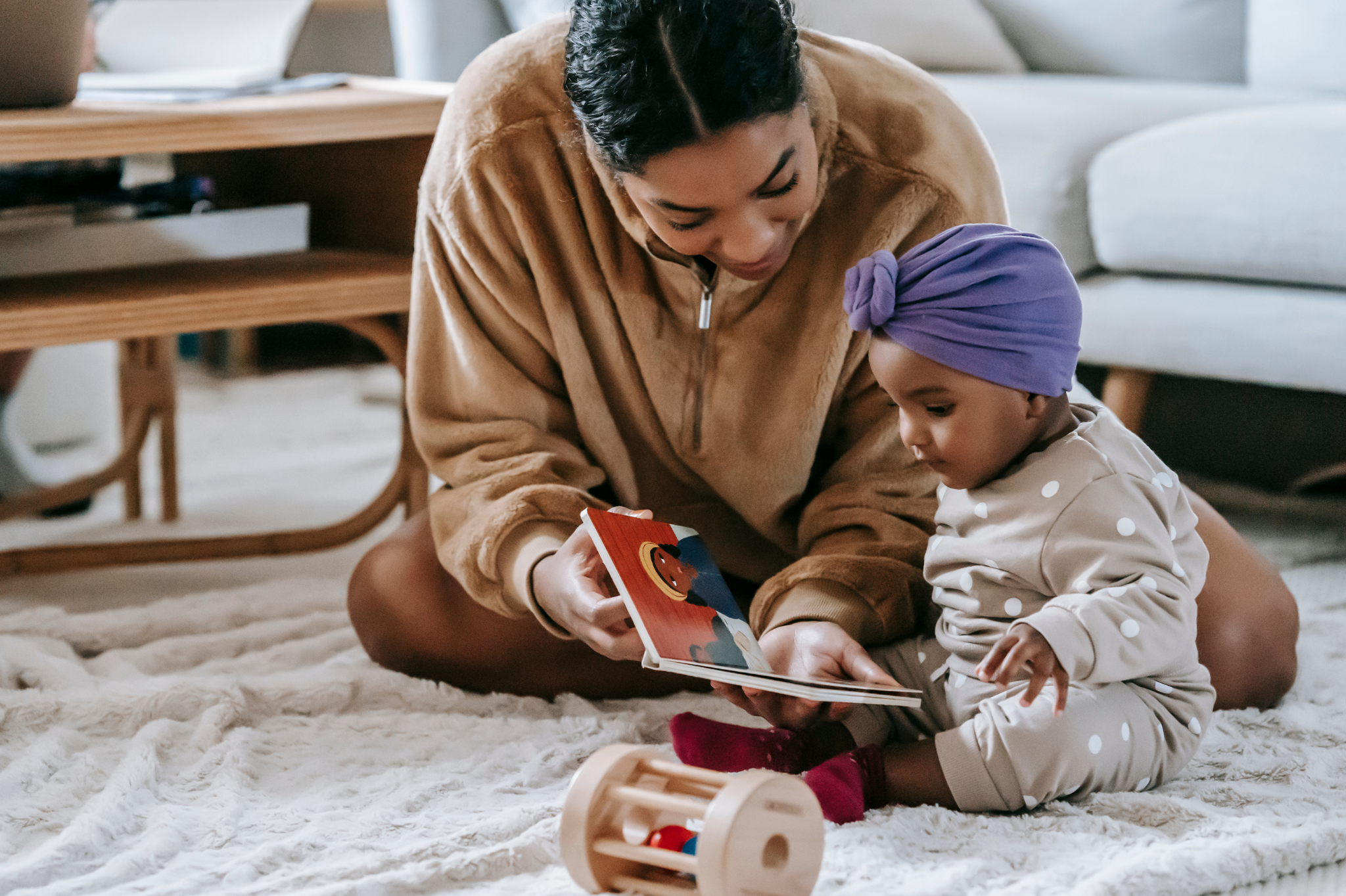 An adult and baby sitting on a soft rug in Portland, Oregon, or Seattle, Washington, reading a colorful children’s book together, symbolizing the importance of nurturing secure connections and emotional attunement in early relationships.