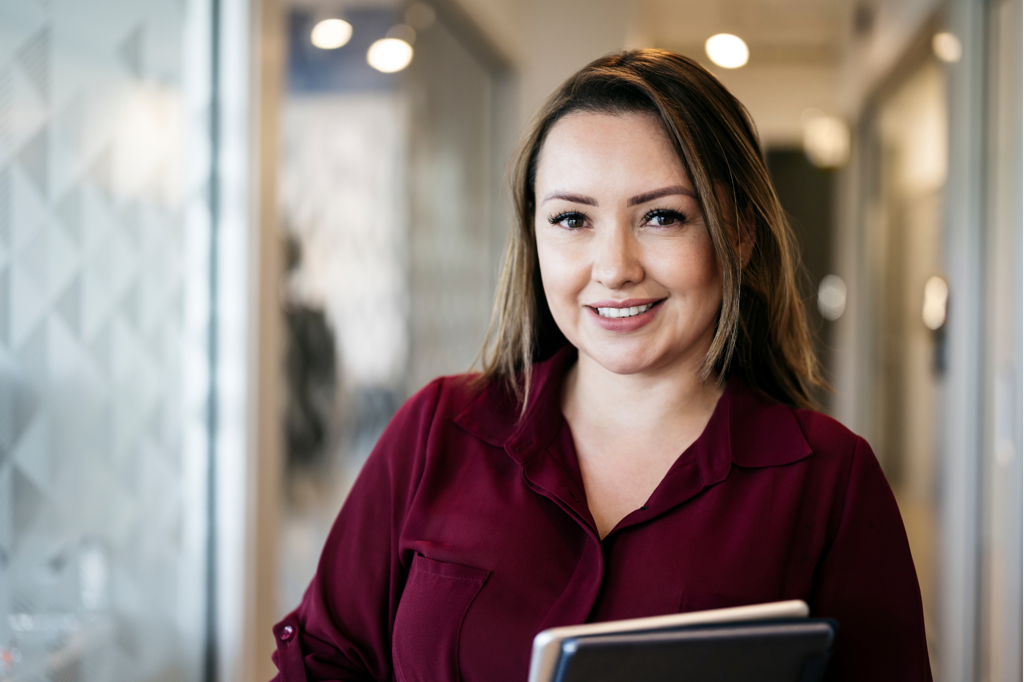 A woman in a maroon blouse holds a tablet, her confident smile showing how stress management in Seattle and Bellevue, Washington can help overcome workplace stress and burnout. 98121, 98052, 98704, 98040, 98039, and 98077.