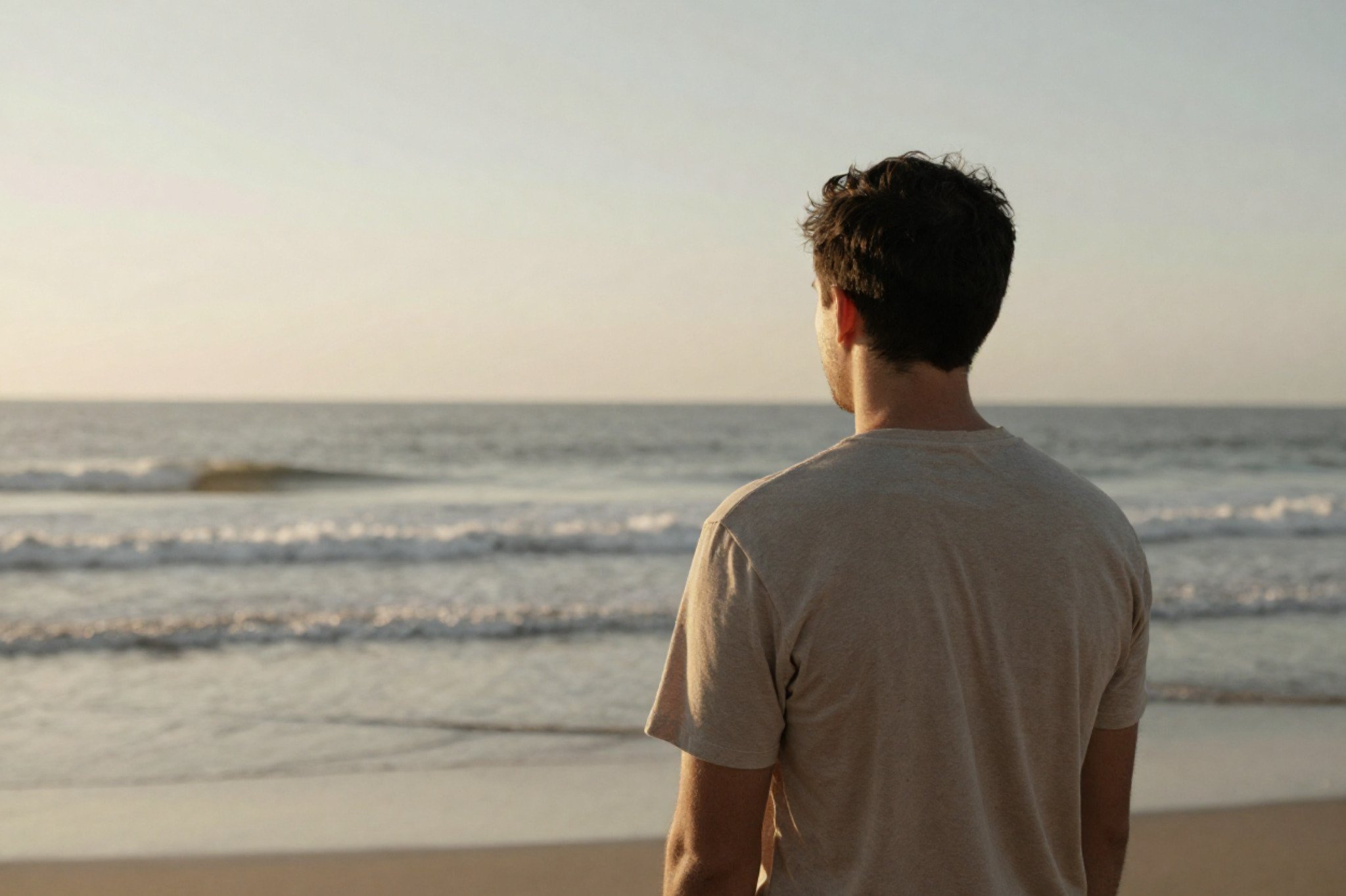A man standing alone facing the calm ocean water. Are you anxious when you wake up? Learn how workplace stress therapy in Seattle, WA can support you.