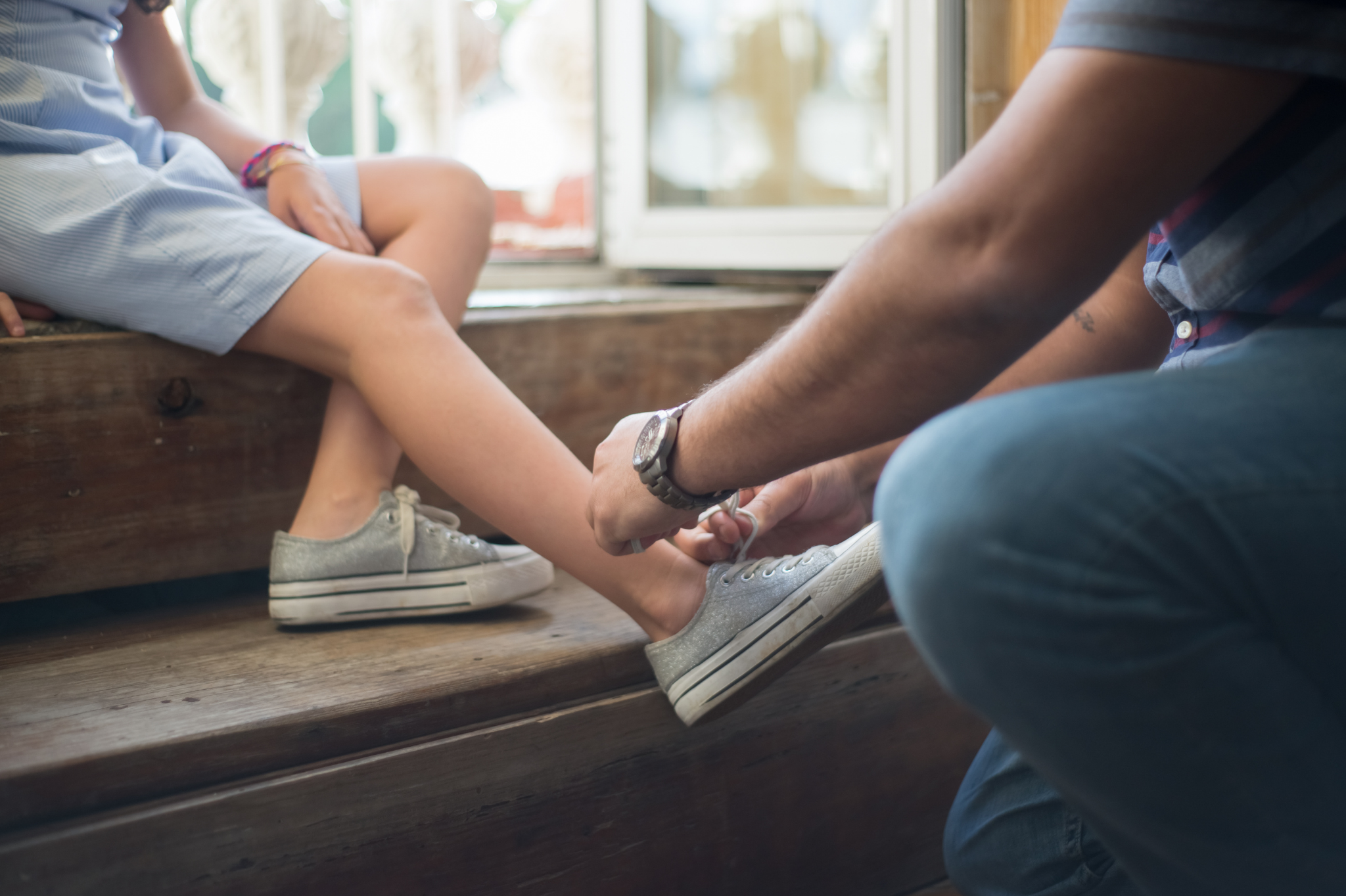 An adult tying a child’s glittery silver shoelaces on a wooden bench in Portland, Oregon, or Seattle, Washington, symbolizing acts of care and support that foster secure attachment and trust in relationships.