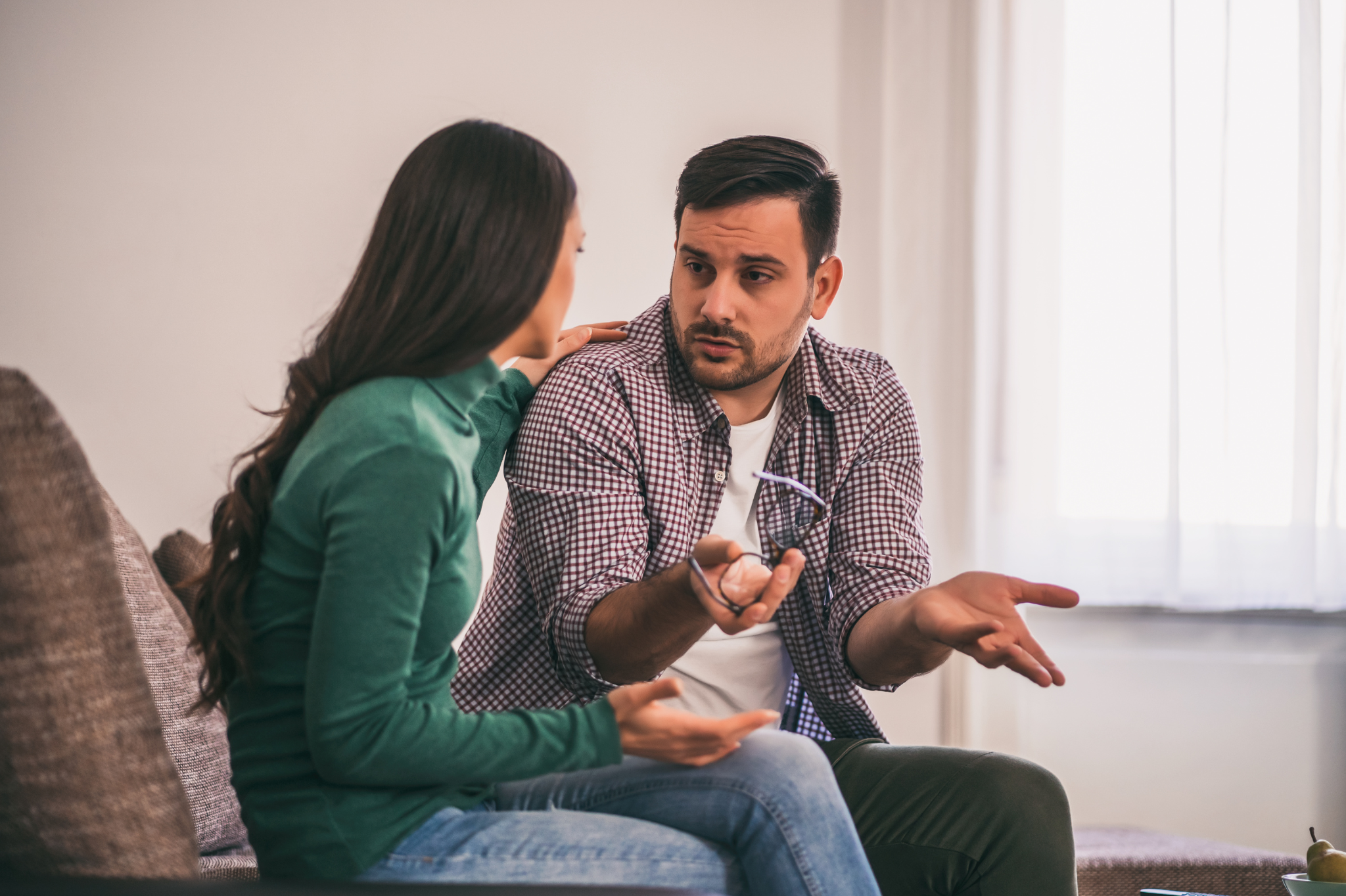 Two people sit on a couch engaged in a serious conversation, reflecting how to stop arguing through couples therapy in Portland, Oregon, serving zip codes 97035, 97229, 97214, and 97210.