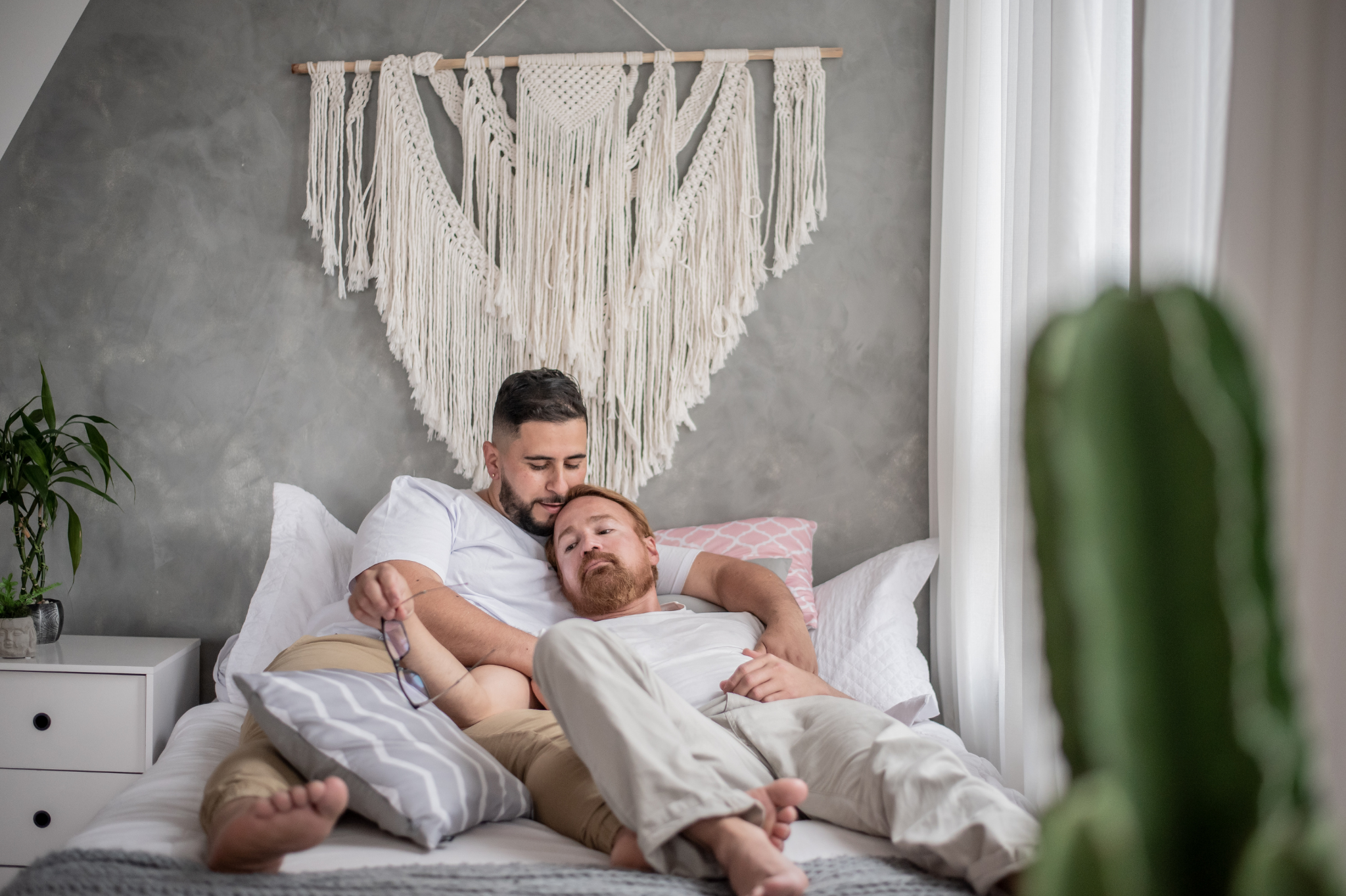 A same-sex couple relaxing together on a cozy bed in Portland, Oregon, or Seattle, Washington, symbolizing the trust, emotional safety, and intimacy that define secure attachment in relationships.