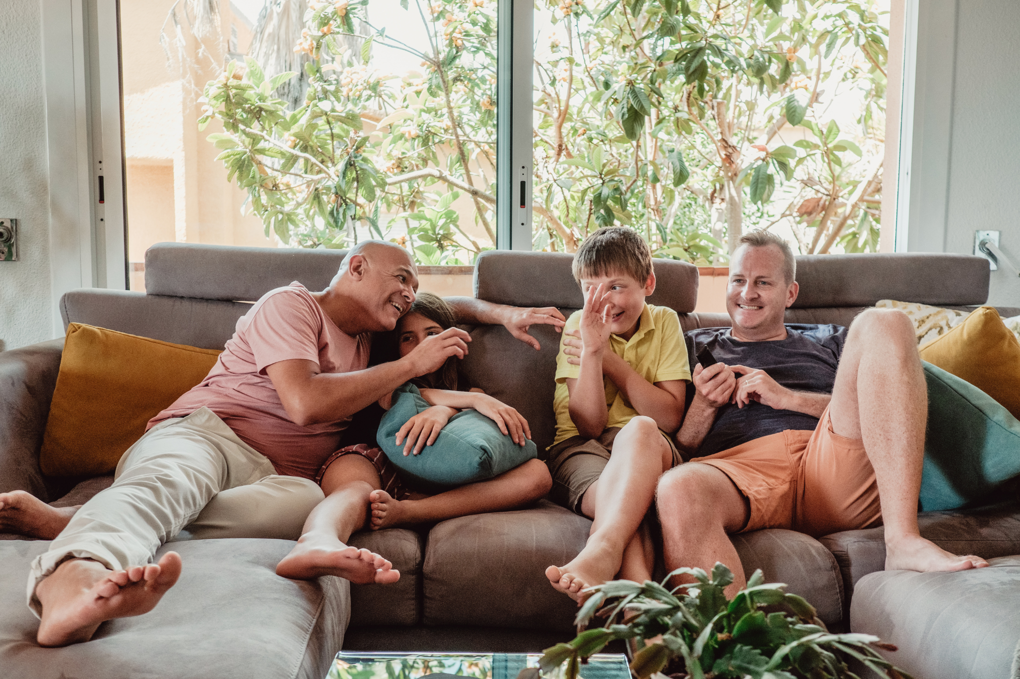 A same sex family gathered on a cozy gray couch highlights moments of connection and relaxation, symbolizing themes of couples therapy, marriage counseling in Portland, Oregon, serving zip codes 97035, 97229, 97214, and 97210.