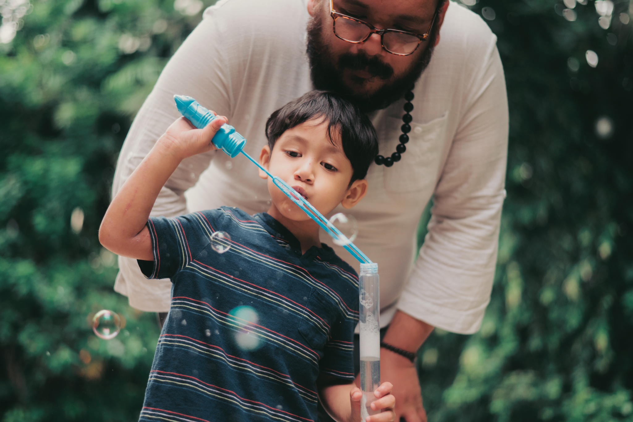 an adult and child blowing bubbles together in a garden in Portland, Oregon, or Seattle, Washington, symbolizing the need for reassurance and connection often experienced in anxious attachment styles.
