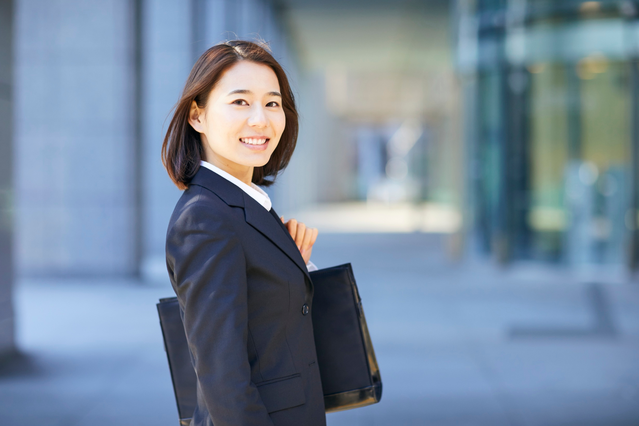 A smiling asian businesswoman holds a briefcase, representing the success possible when you manage workplace stress and burnout. Find effective stress management in Seattle and Bellevue, Washington, serving zip codes 98004, 98006, 98109,