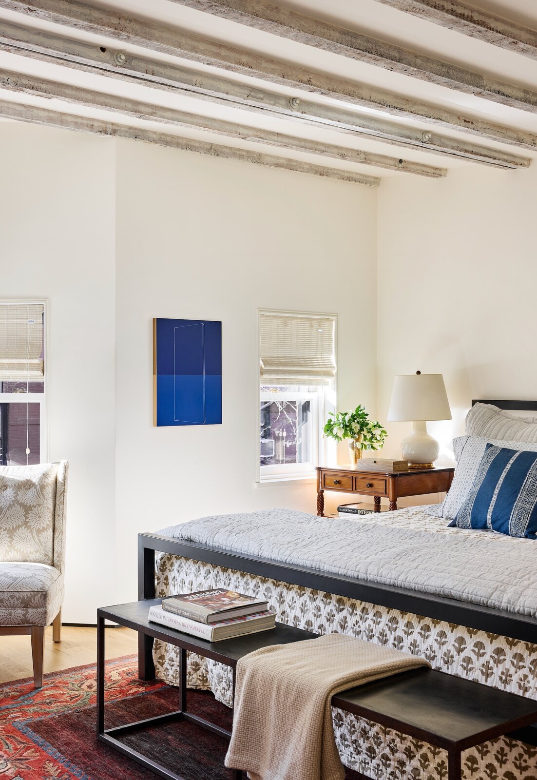  The primary bedroom has small windows but lofty ceilings with original exposed beams. The comforter is from Out of Hand in Great Barrington, Massachusetts, the table lamp is by Christopher Spitzmiller, and the vintage rug came from a dealer in Cleve