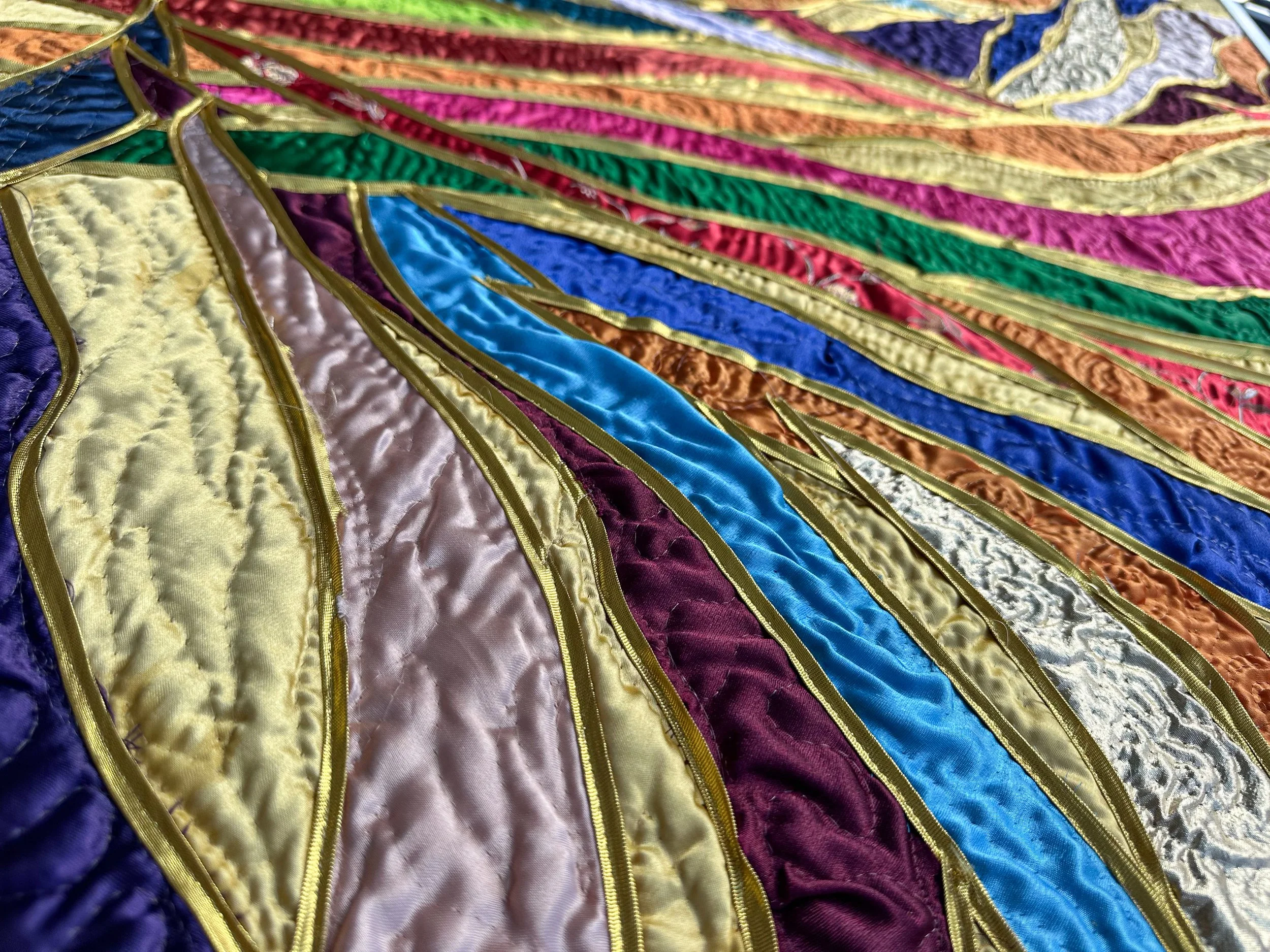 Colorful fiber art piece with intricate stitched patterns and gold-colored borders.