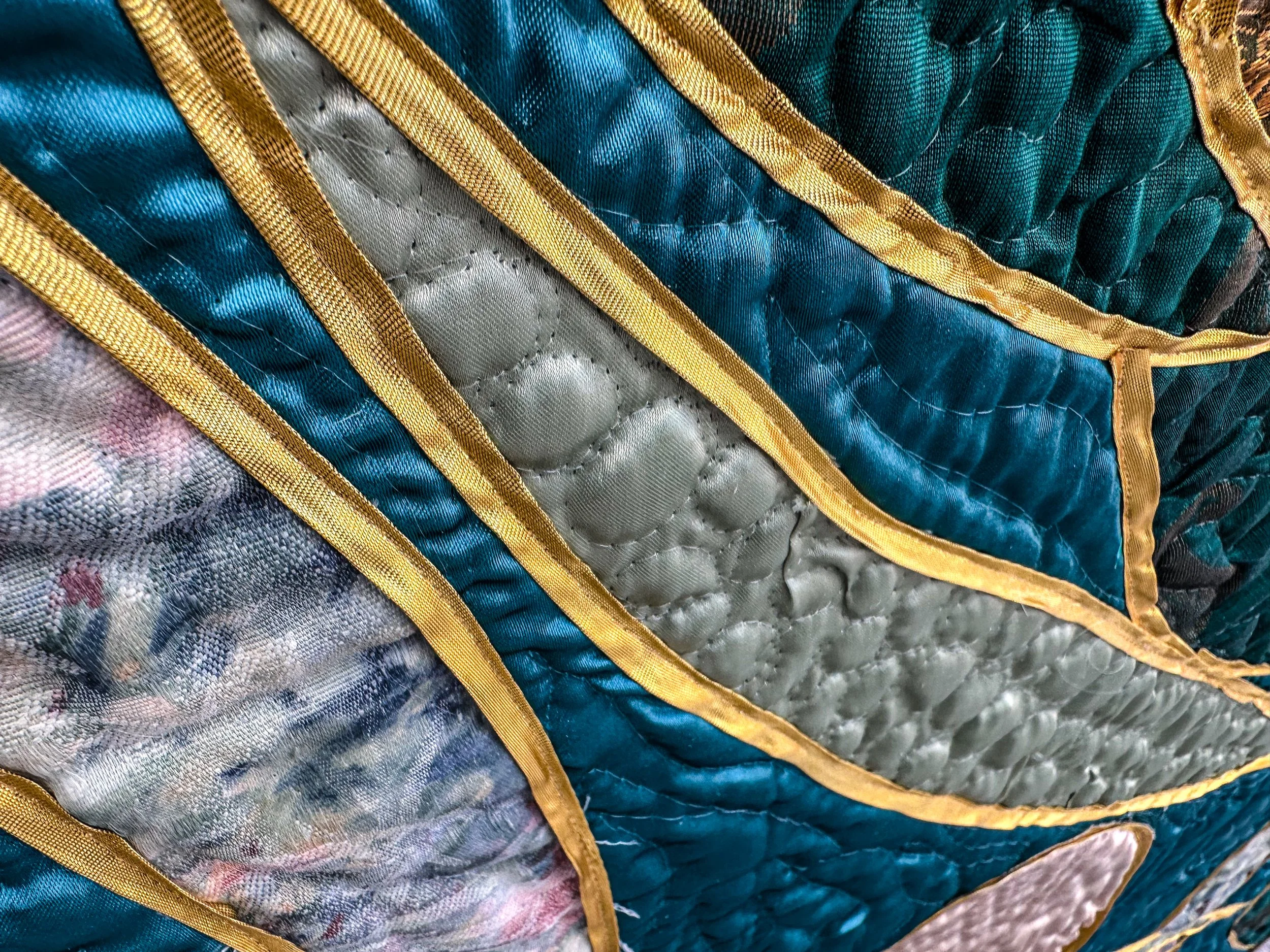 Close-up of colorful fiber art piece with gold ribbon and quilted stitching.