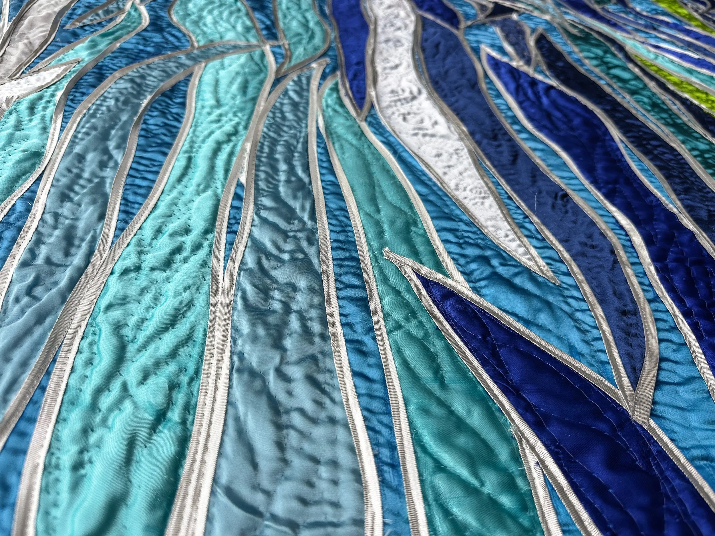 Close-up of an embroidered fiber art with blue, teal, white, and green threads creating a vibrant, textured pattern.
