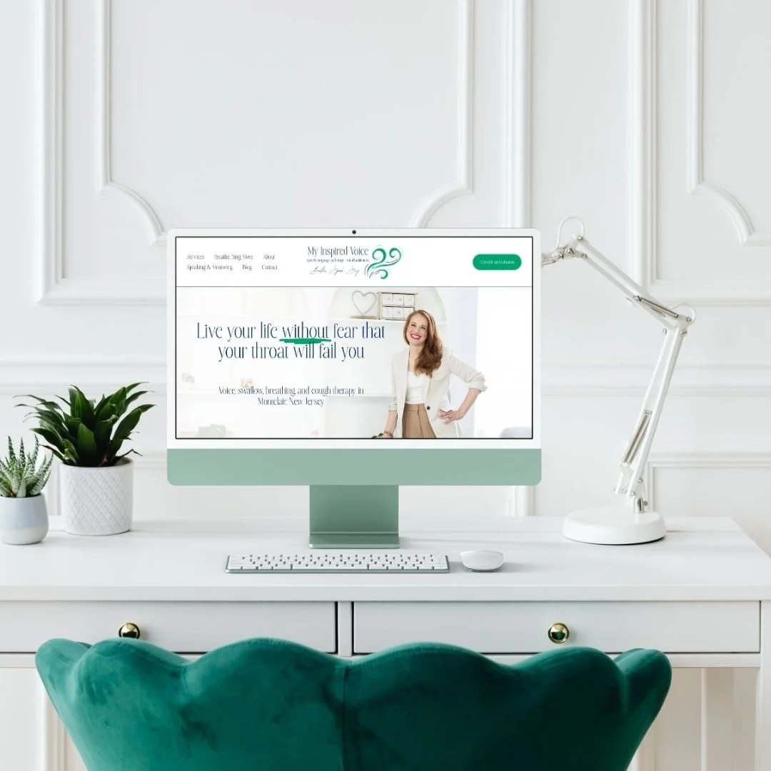 Desk with computer and teal chair with website for voice specialist.
