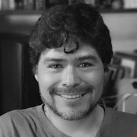 Una persona sonriendo con barba y cabello oscuro, en un entorno interior.