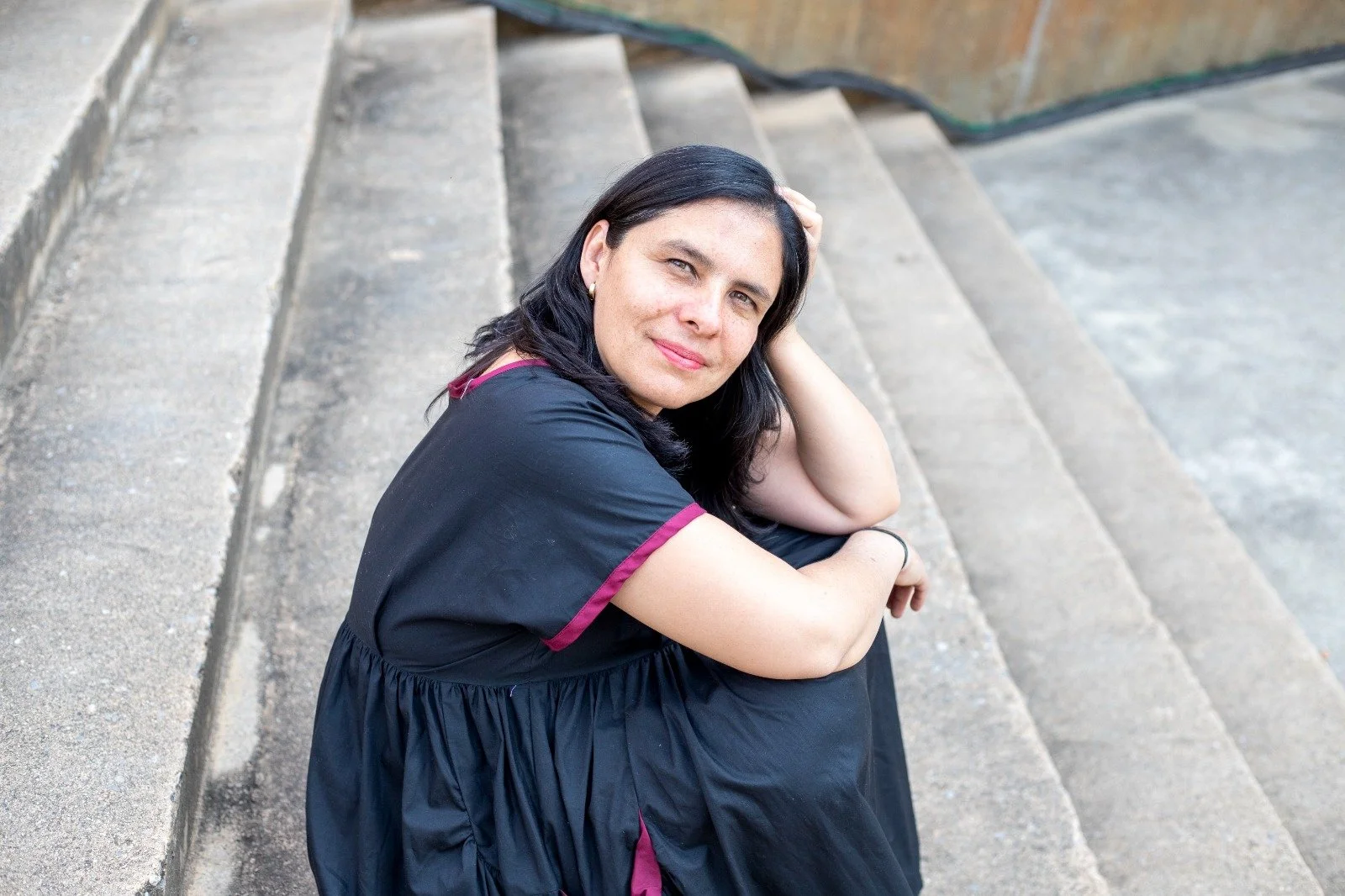 Mujer con vestimenta de graduación sentada en las escaleras de concreto, mirando a la cámara.