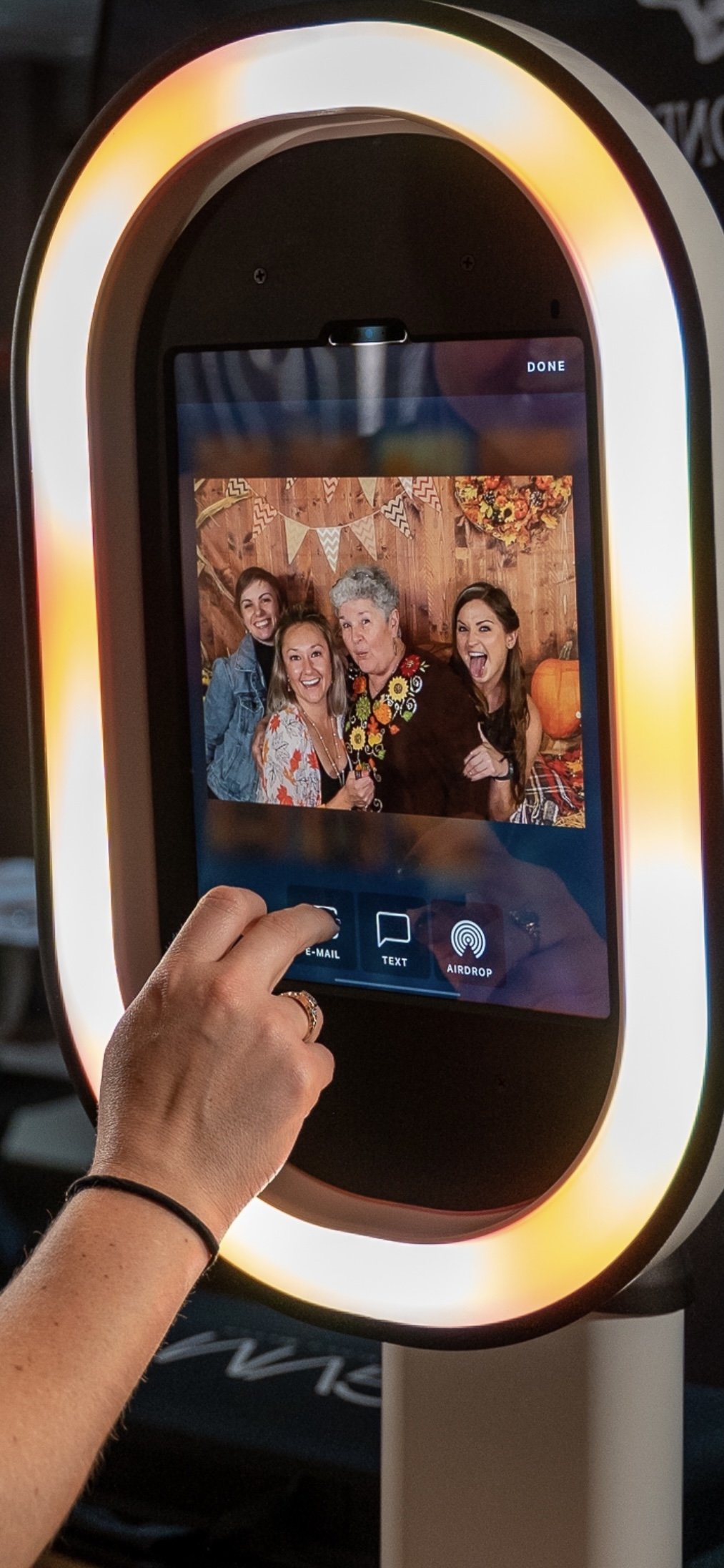A photo booth screen showing a picture of four women smiling and making funny faces, with some decorative bunting and a pumpkin in the background.