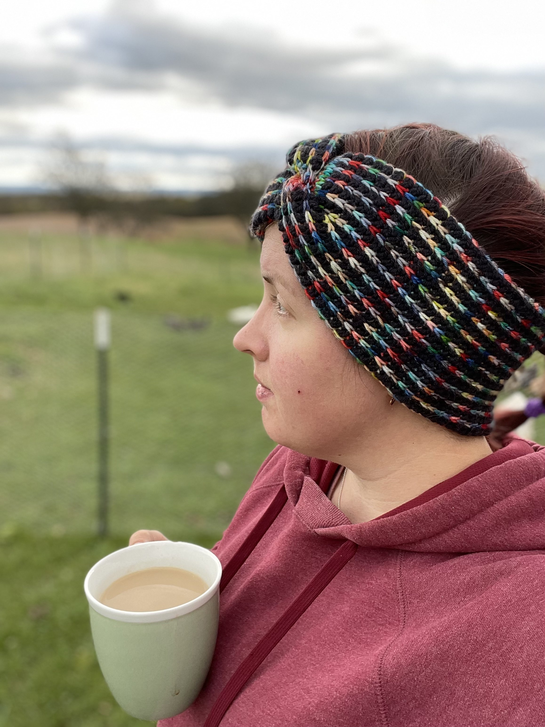 Ruth gazes peacefully off into the distance while wearing the Medusa Earwarmer. It is an alternating black and multi-colored stripe pattern running around the circumference of hear head. The ear warmer meets in a faux-knot over her eye