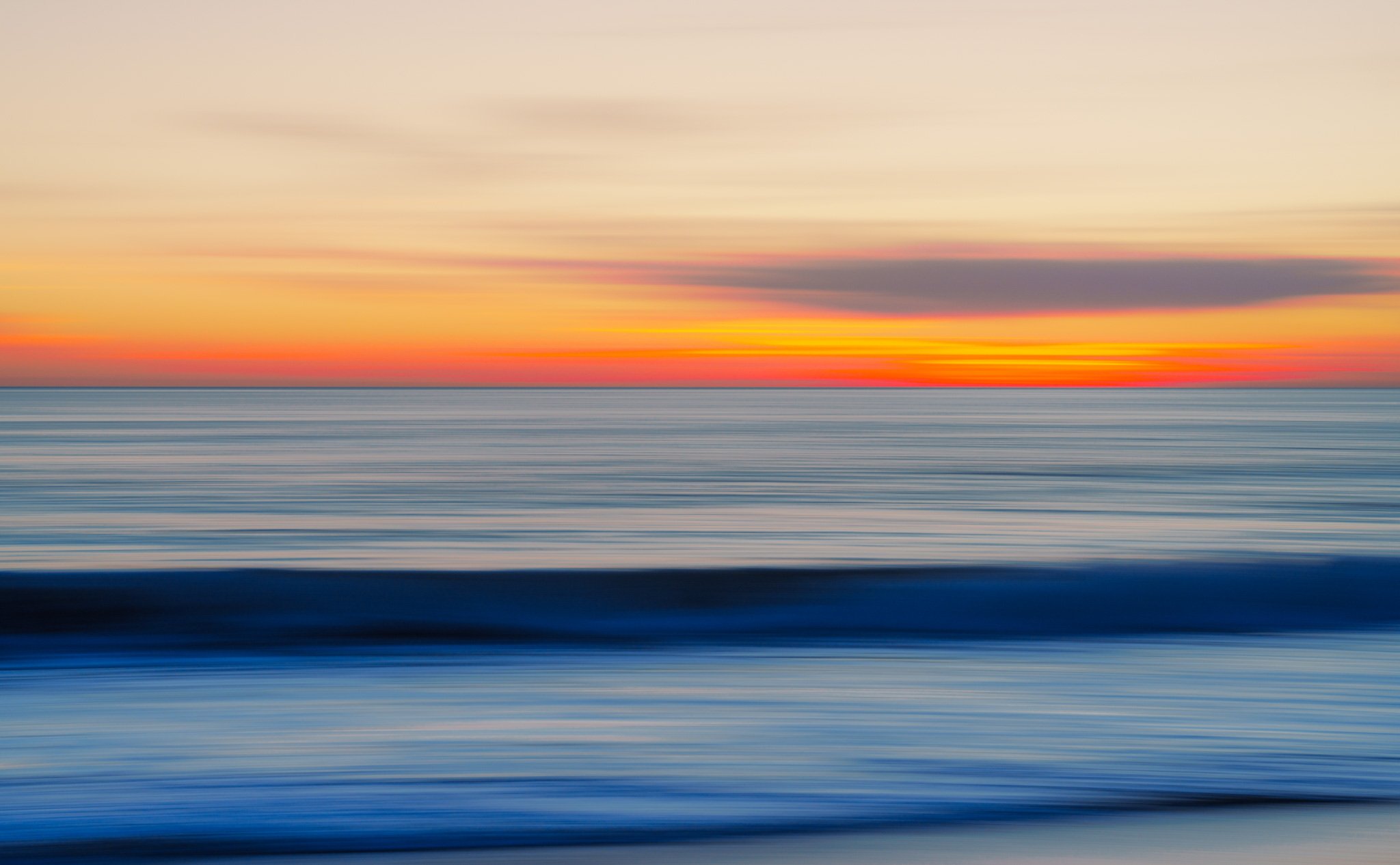 a deep orange sunset splattered with pastel pink hues set against a blurred baby blue ocean.