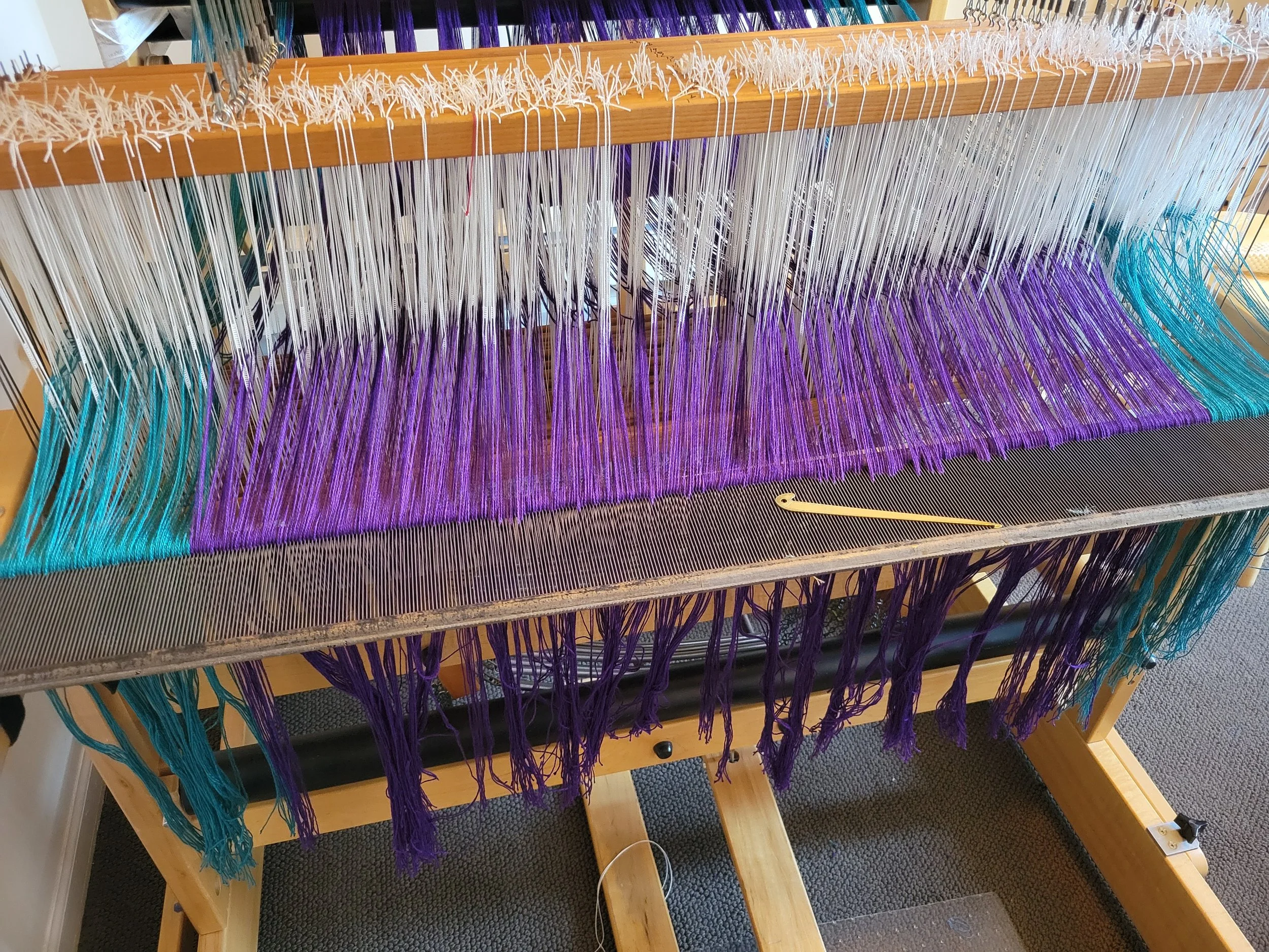 Each warp end is threaded through the openings in a "reed" that will beat each line of cloth onto the grid.