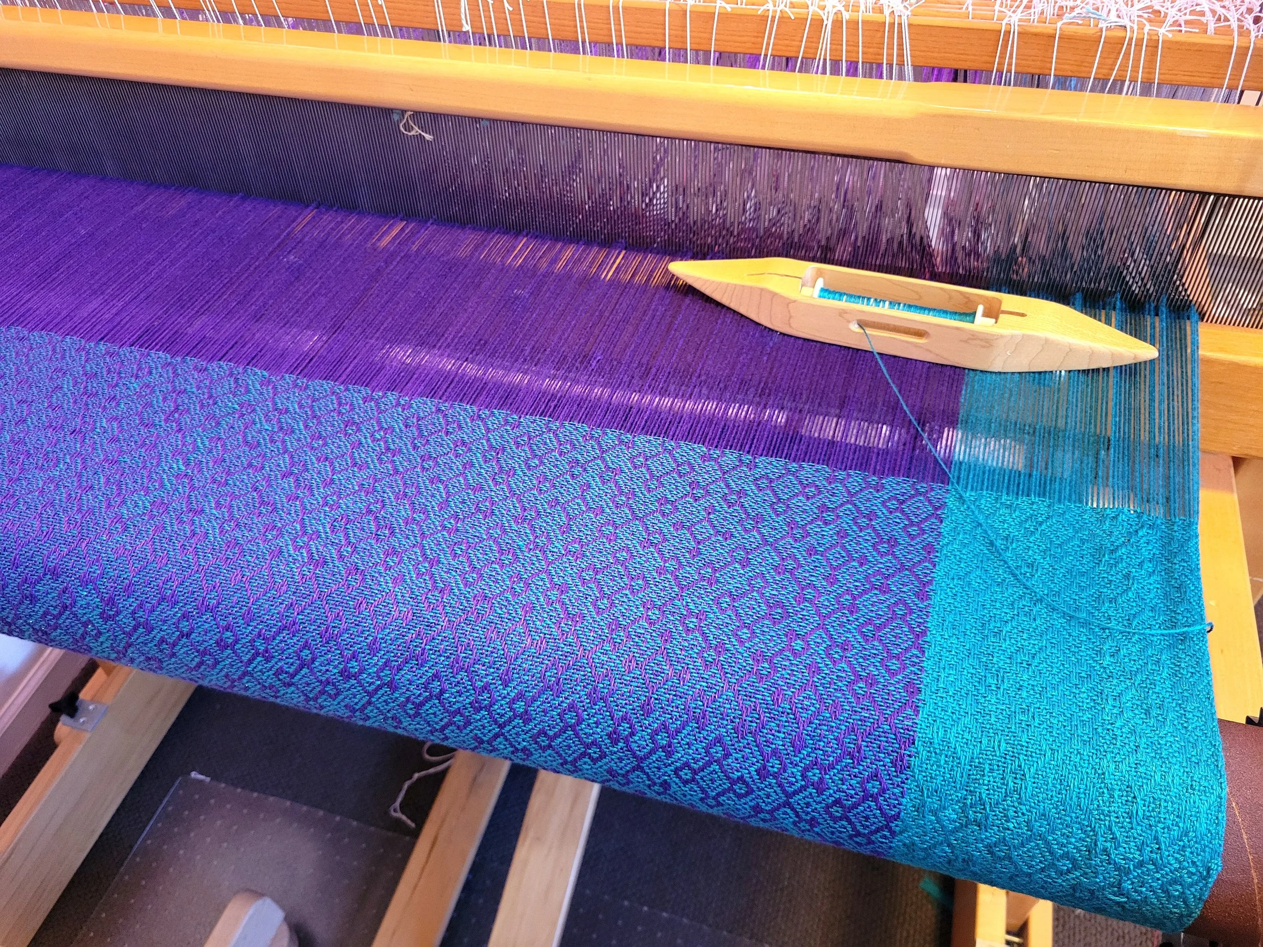 A shuttle holds the weft threads that weave between the lifted and lowered warp threads.
