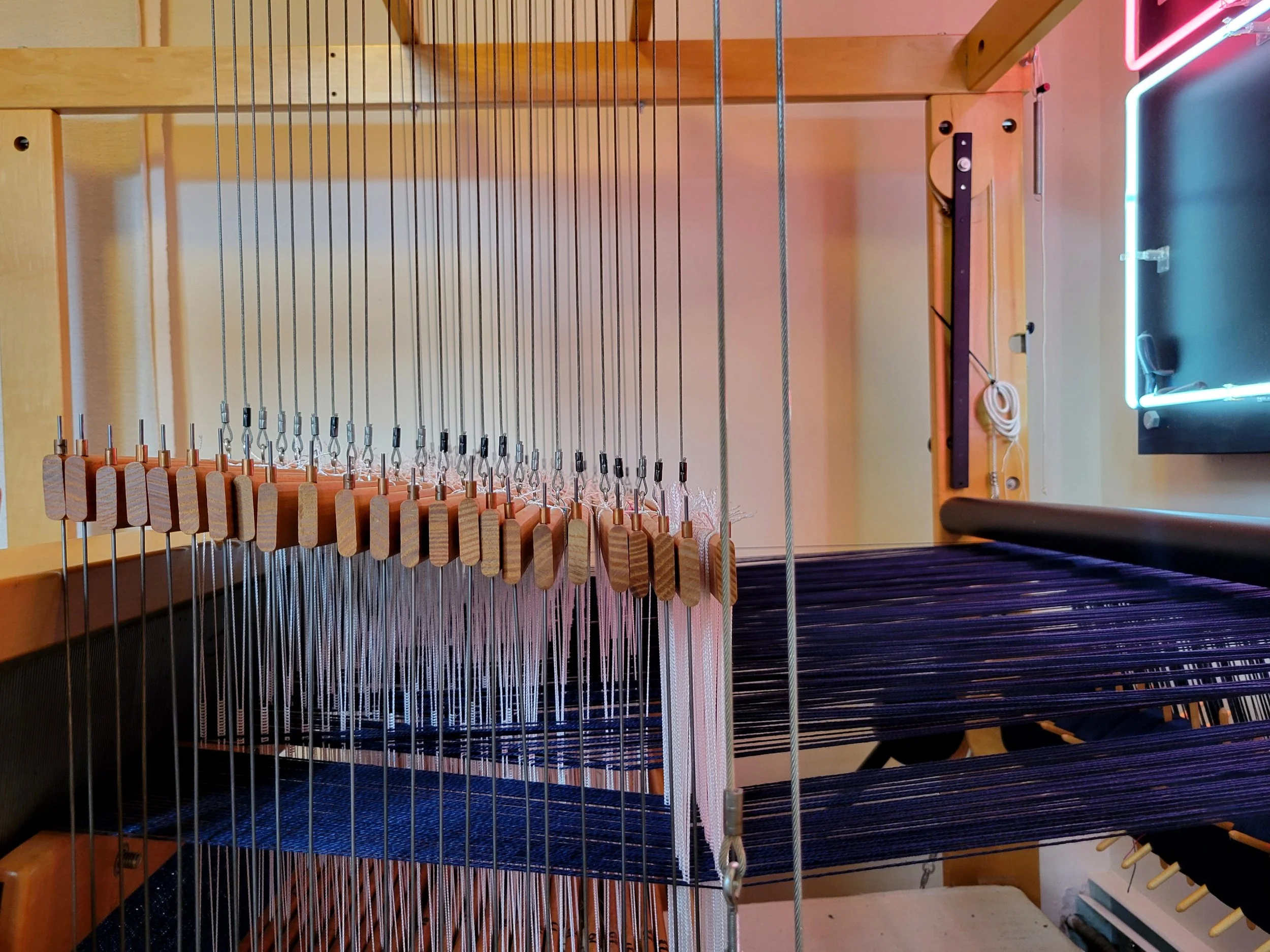 Warp threads going through the harnesses and reed, where they are lifted and lowered according to the pattern.