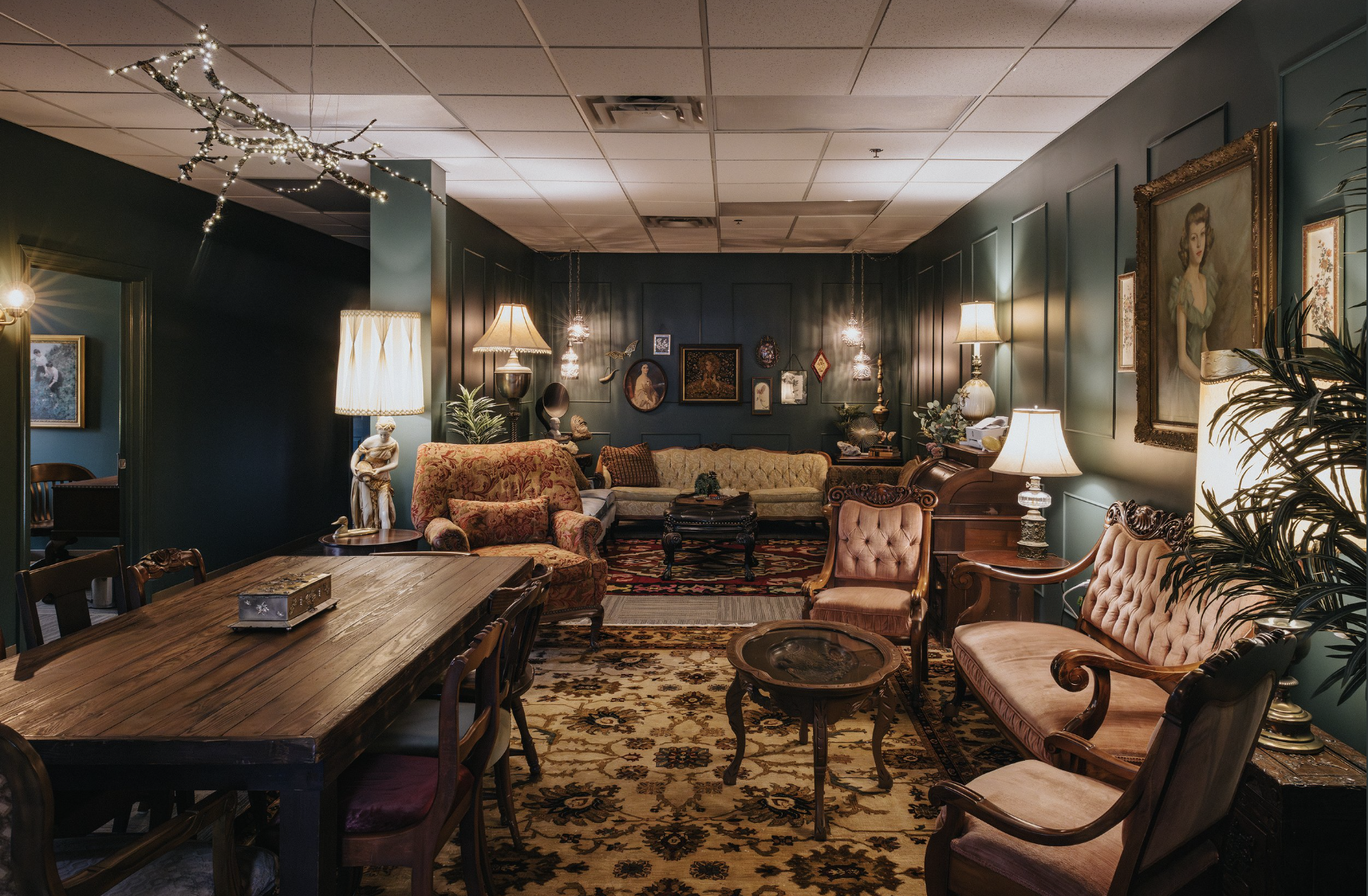 Vintage-style room with antique furniture, wooden table, upholstered chairs, sofas, lamps, wall paintings, and decorative items.