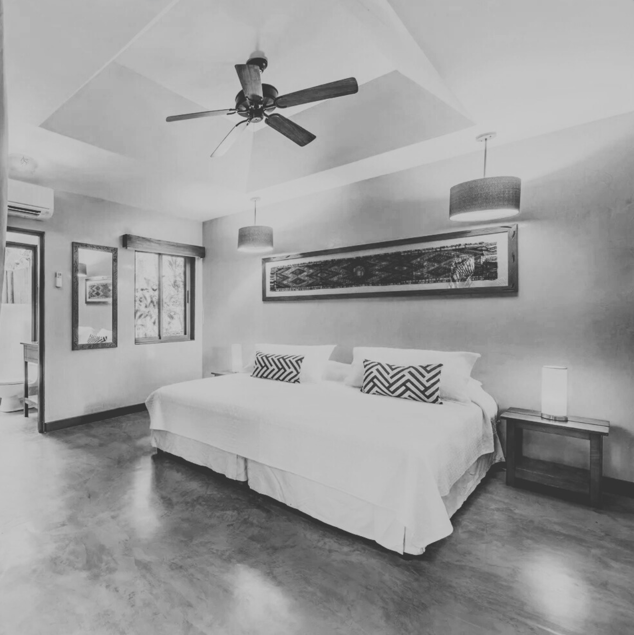 A hotel room with a king-sized bed, nightstands, and lamps, in a warm color scheme with tropical decor, with a view into a bathroom through a partially open door.