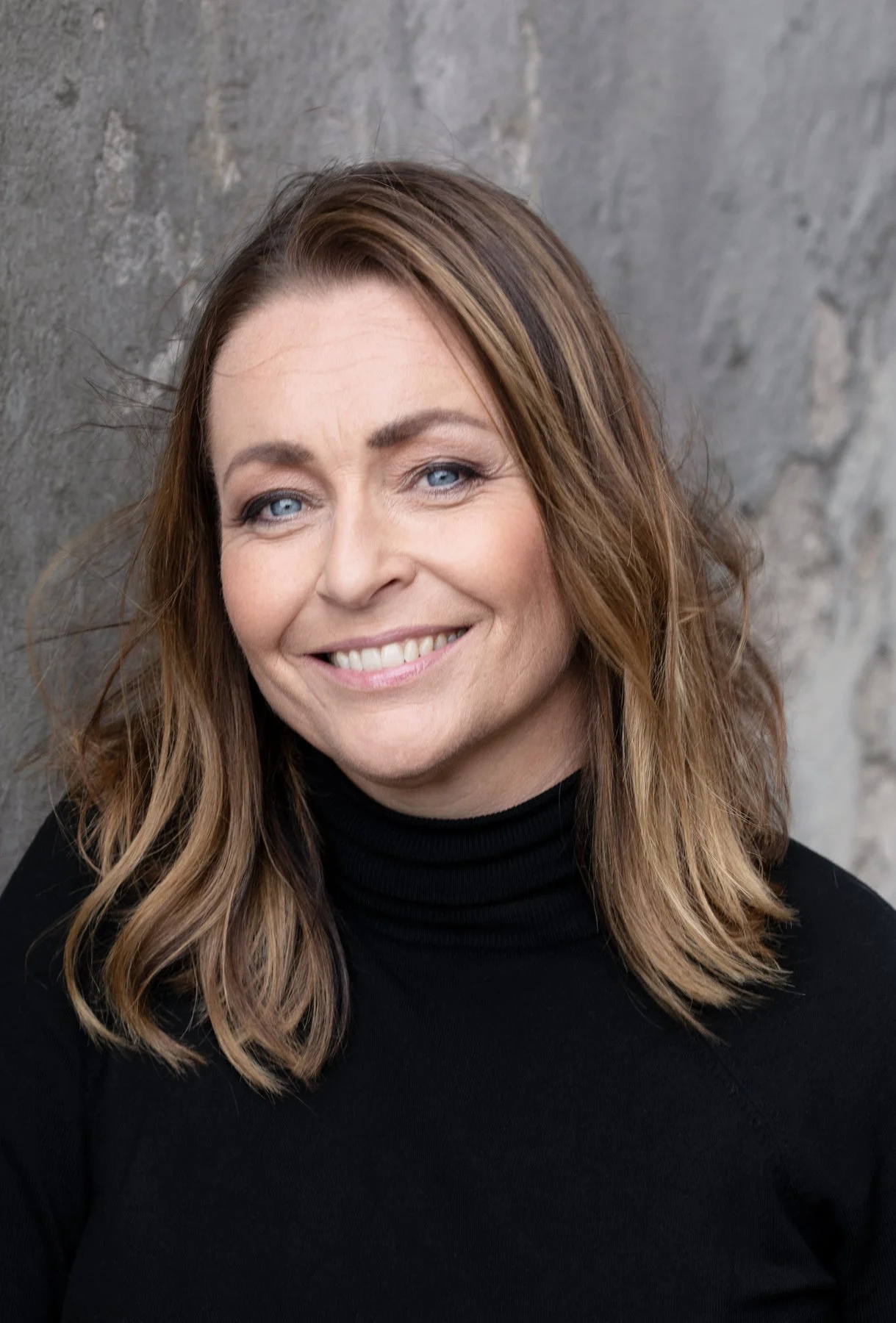 Bild på Sophie Strömberg med svart polotröja som blickar mot kameran, med en grå cemetvägg i bakgrunden