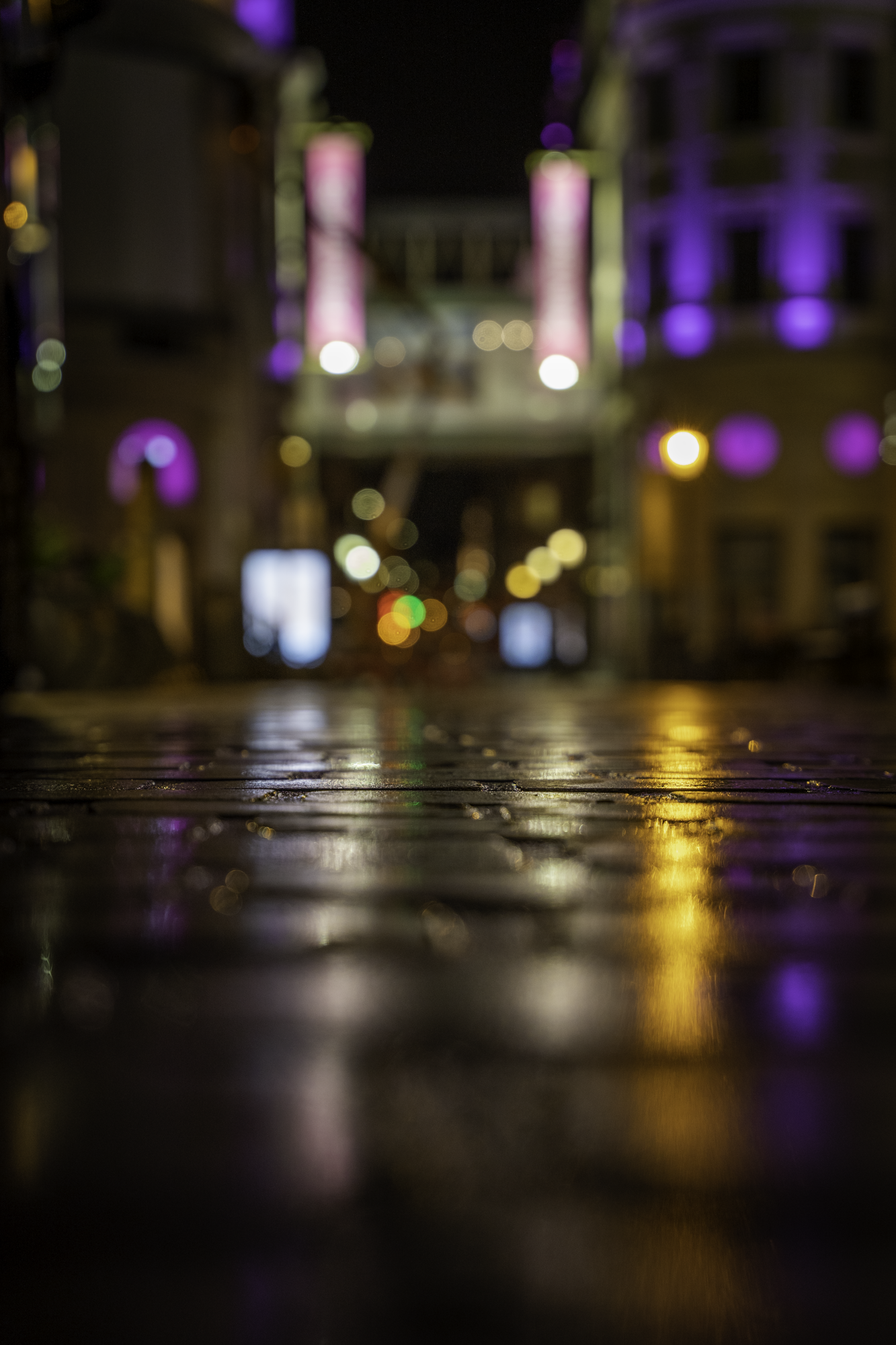 Rue pavée la nuit avec reflets lumineux violets et dorés.
