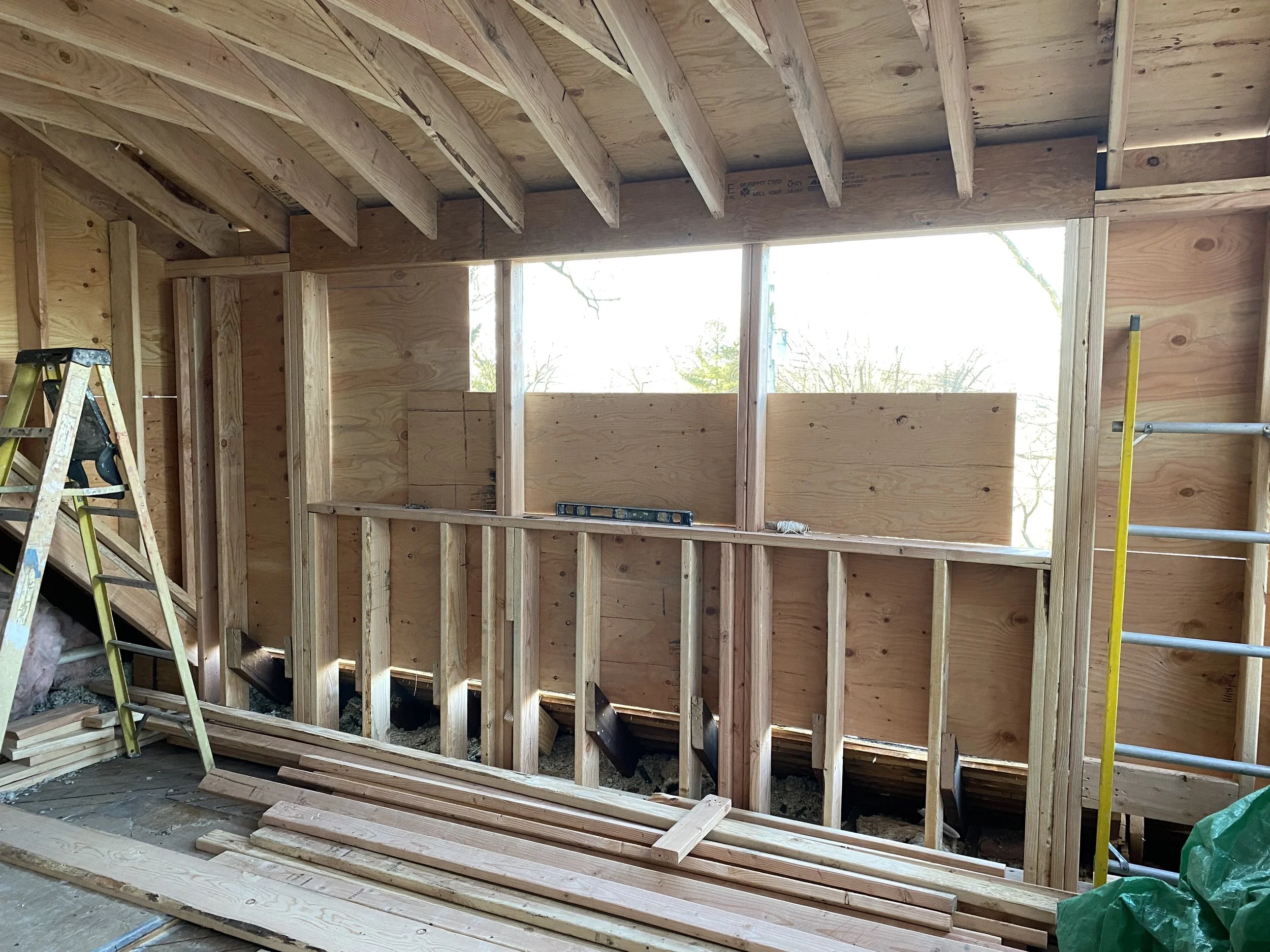 Interior of a house under construction with exposed wood framing, a ladder, and construction tools.