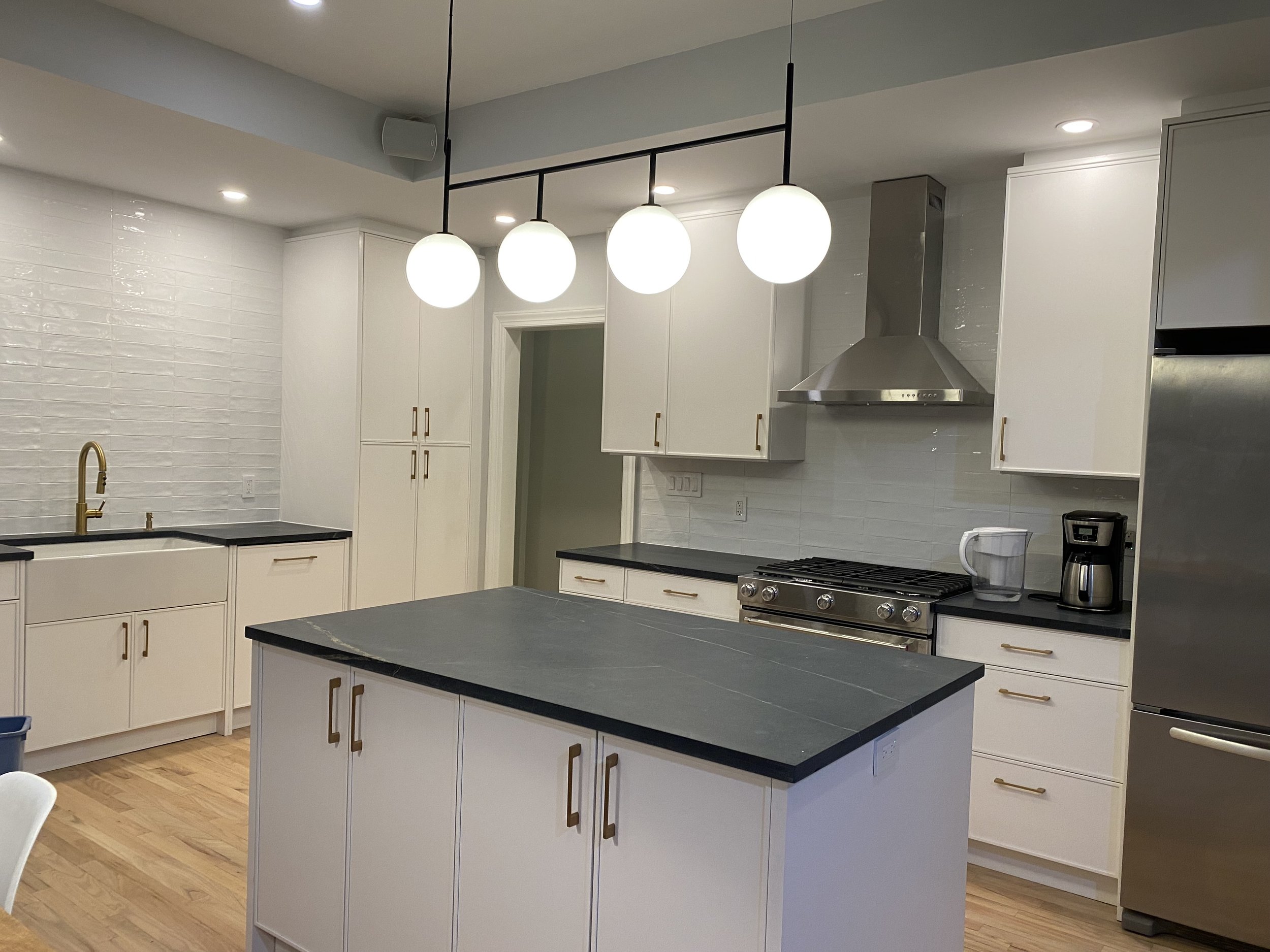 Modern kitchen with white cabinets, black countertops, a central island, stainless steel appliances, a range hood, and hanging globe lights.