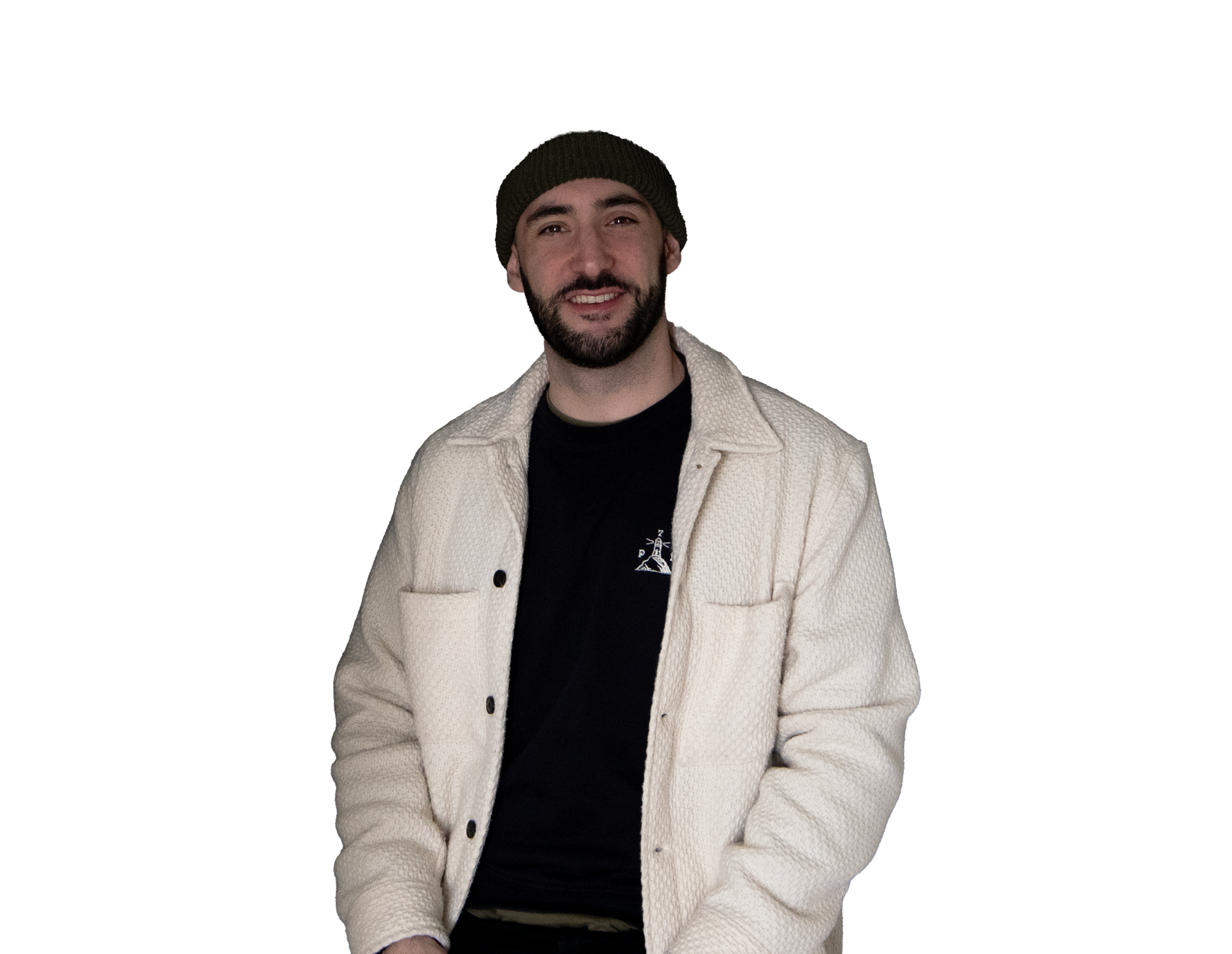 Un homme souriant portant un bonnet vert foncé, une surchemise blanche texturé et un pull bleu foncé, debout.