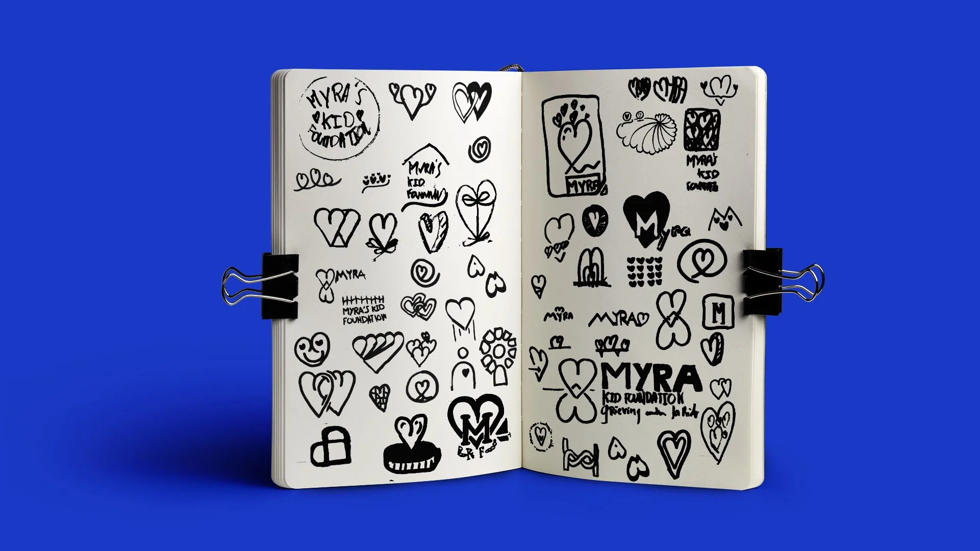 Carnet ouvert avec de nombreux croquis au marqueur noir. Représentant des tentatives de logos utilisant un coeur pour Myra's Kid Foundation sur un fond bleu.