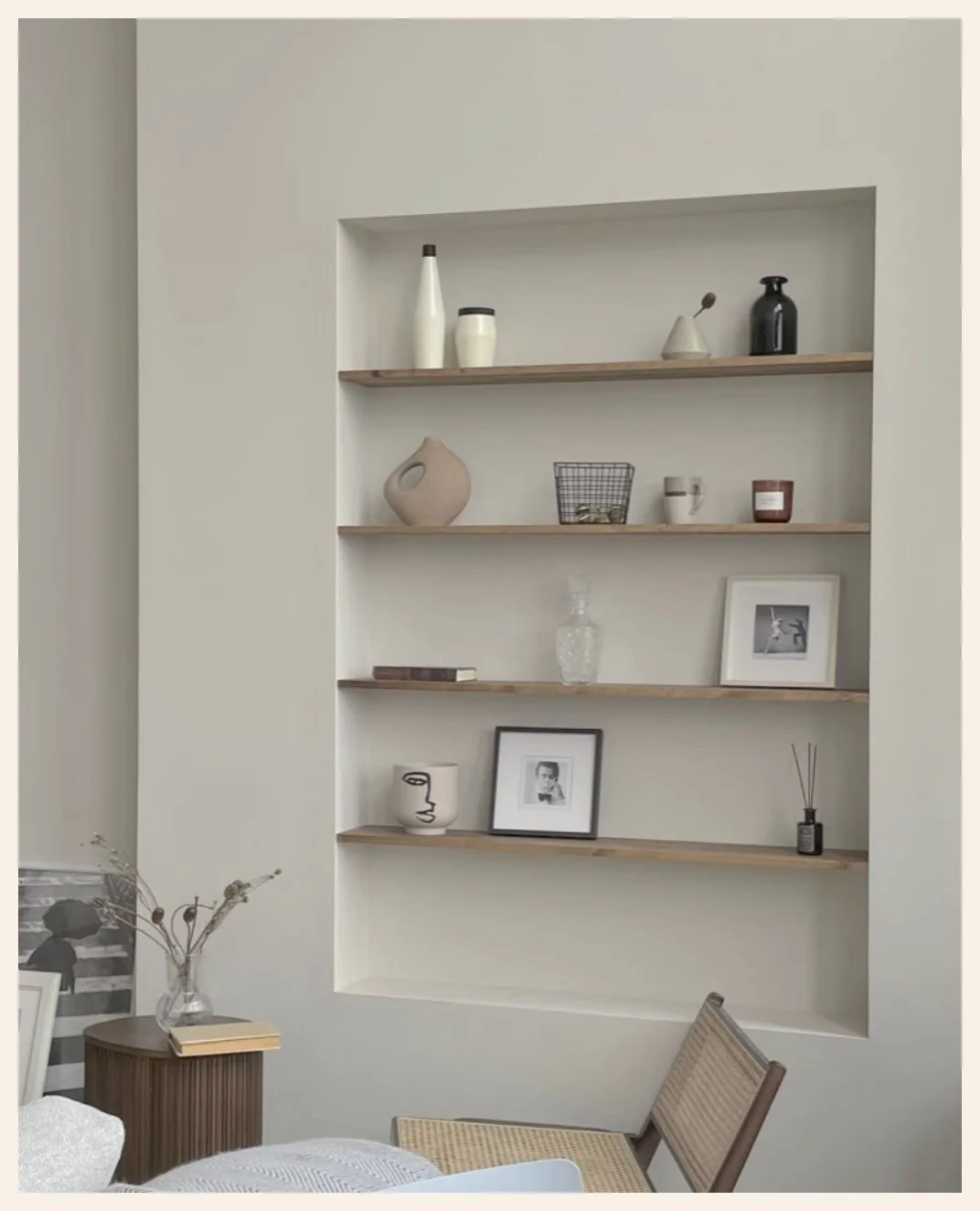 A built-in wall shelf with minimalist decor items, including vases, framed photos, a book, and decorative objects, in a modern interior.