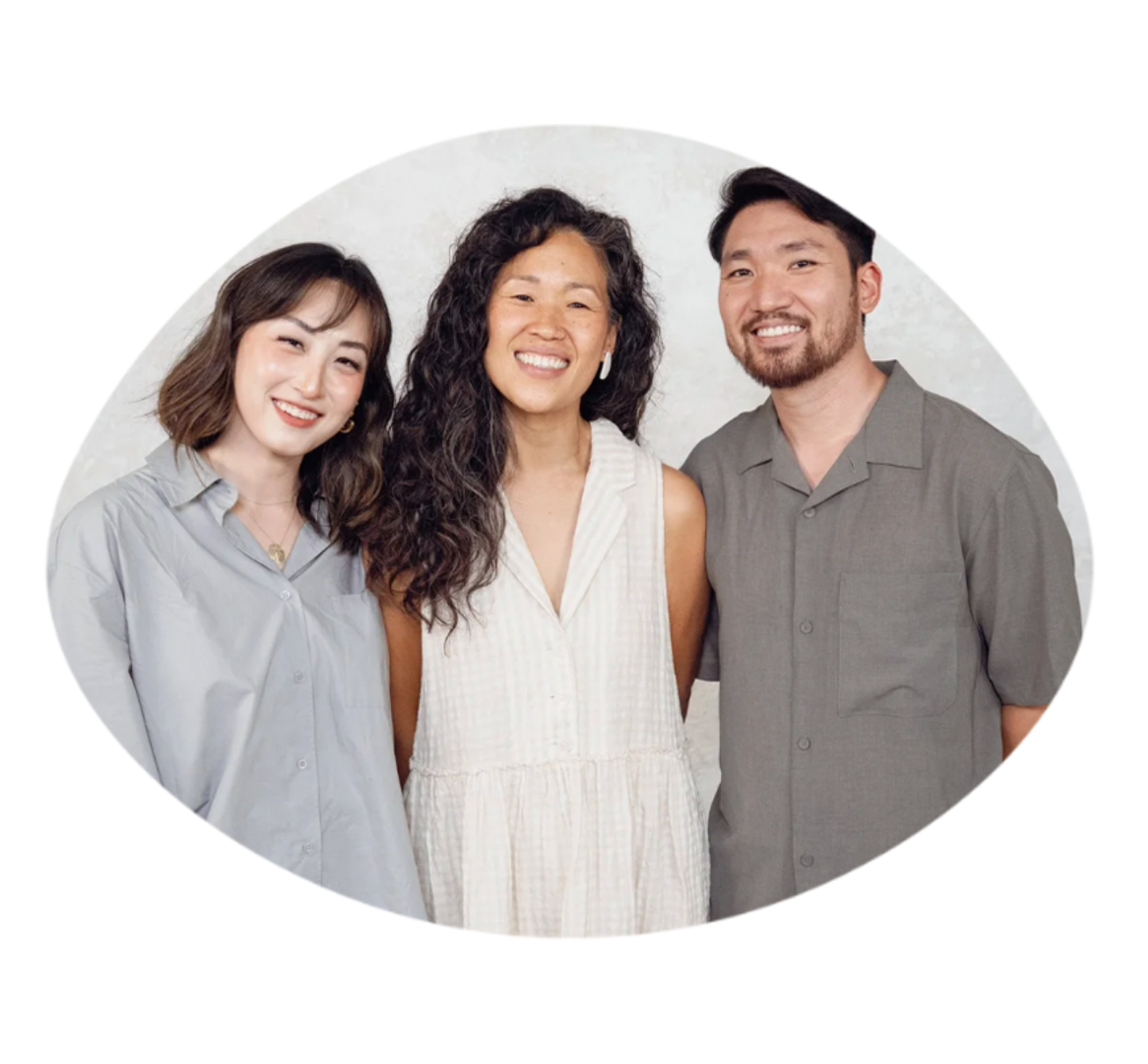 Three smiling people standing close together, two women and one man, in front of a plain background.