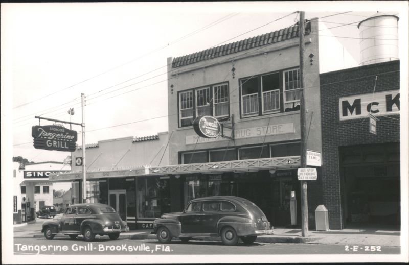 The front of 24 N Broad St can be seen in between the Sinclair Gas Station and the Murphy's Drug Store. Notice the Spencer's Tangerine Grill sign out front!