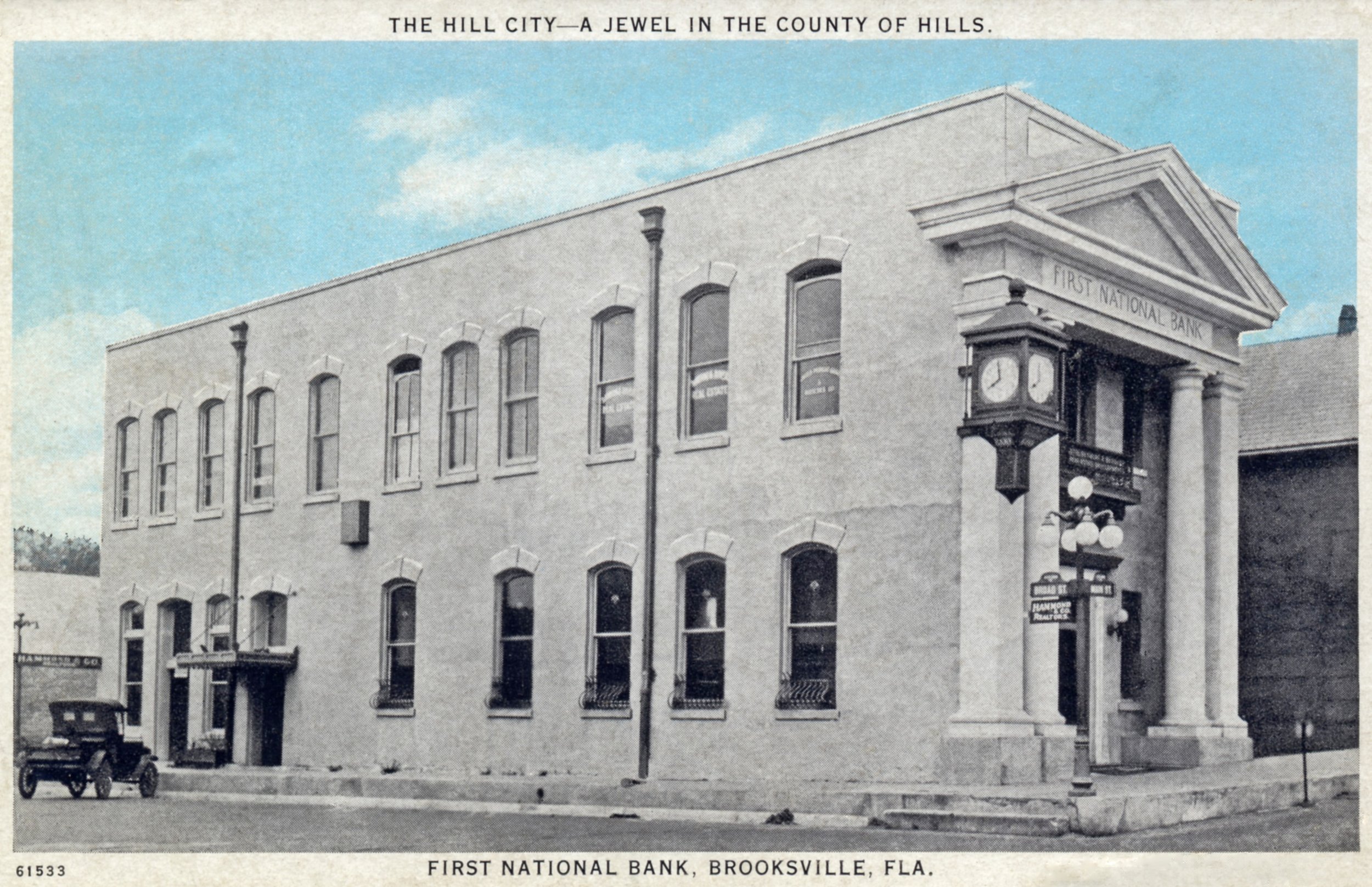 Black and white photo of the First National Bank building in Brooksville, Florida, with a clock on the corner and a street lamp in front of it.