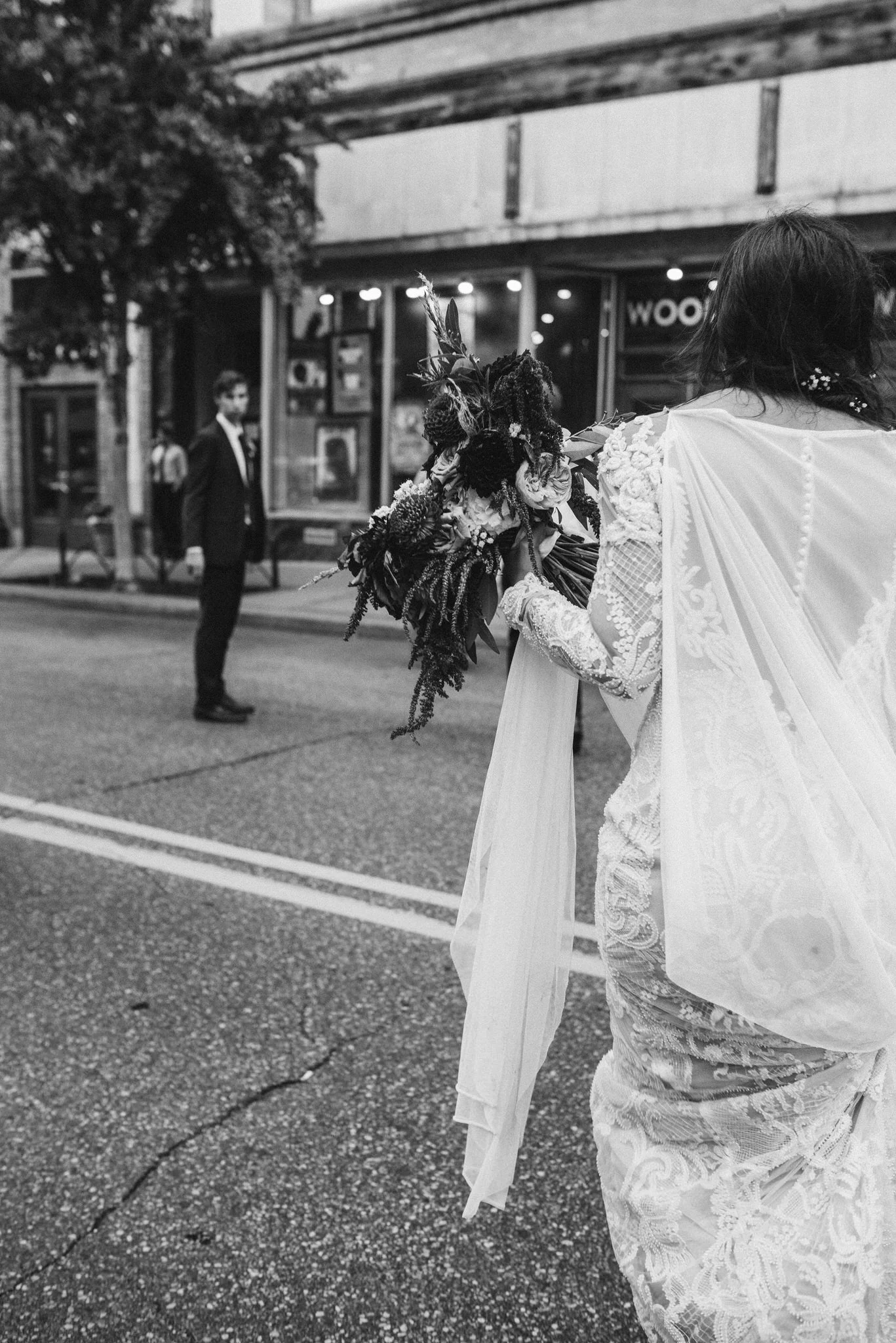 A bride in a wedding dress holding a bouquet facing her groom in a suit on a city street outside of their wedding venue the Teachout Building in the East Village in Des Moines.
