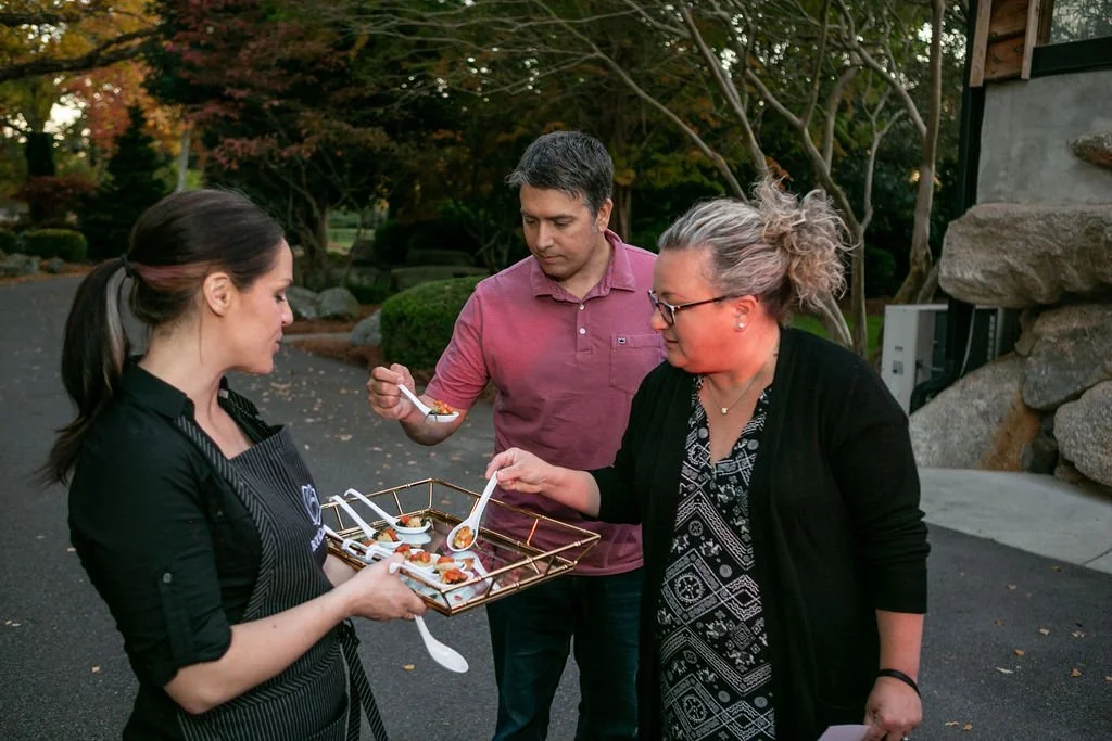Three people outdoors, one holding a tray of appetizers, engaging in conversation.