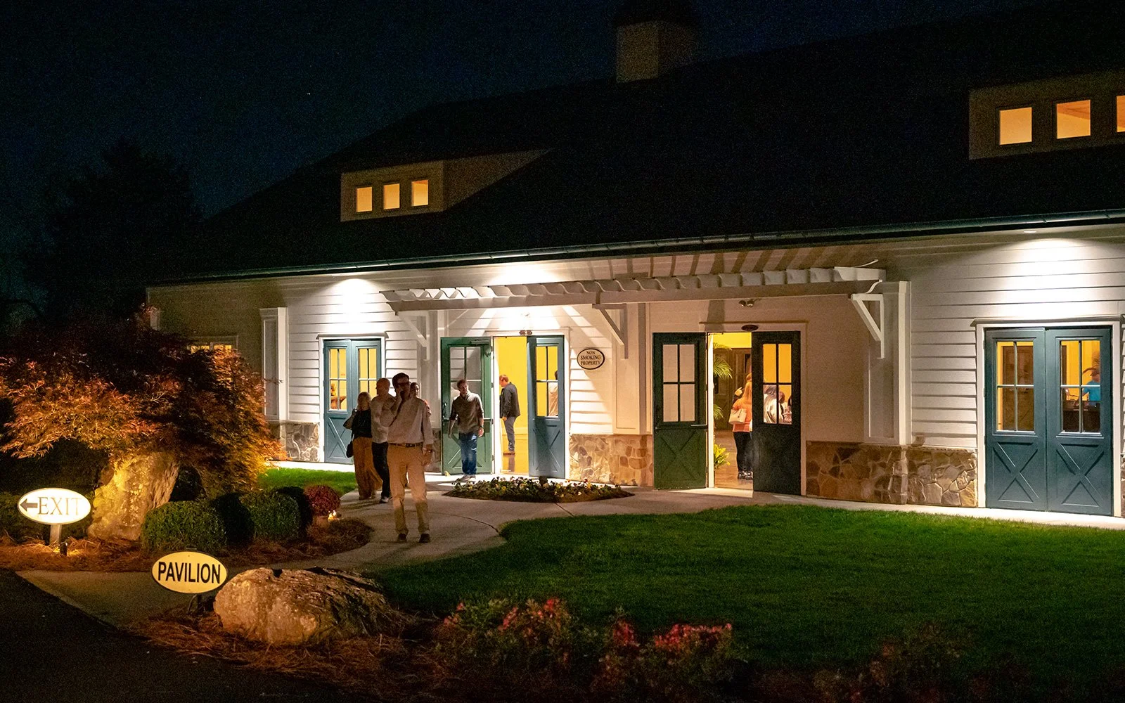Exterior of a pavilion with people exiting at night, illuminated by outdoor lighting.