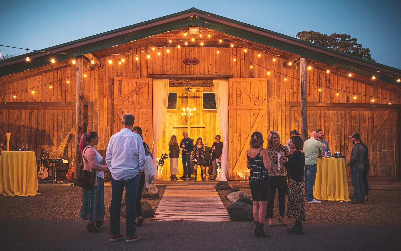 Outdoor barn event with people socializing, string lights, and wooden building.