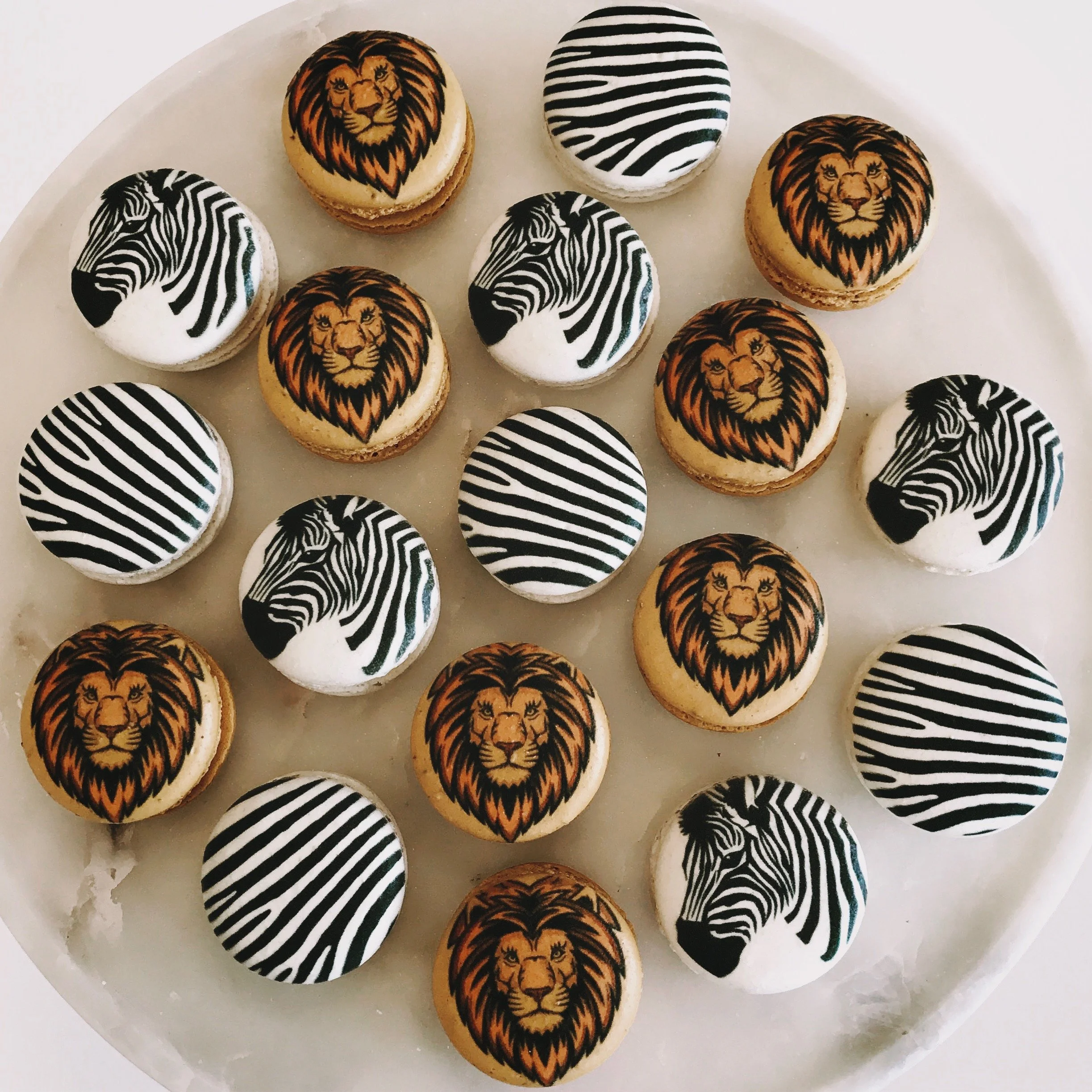 Decorated macarons with lion and zebra designs on a white plate.