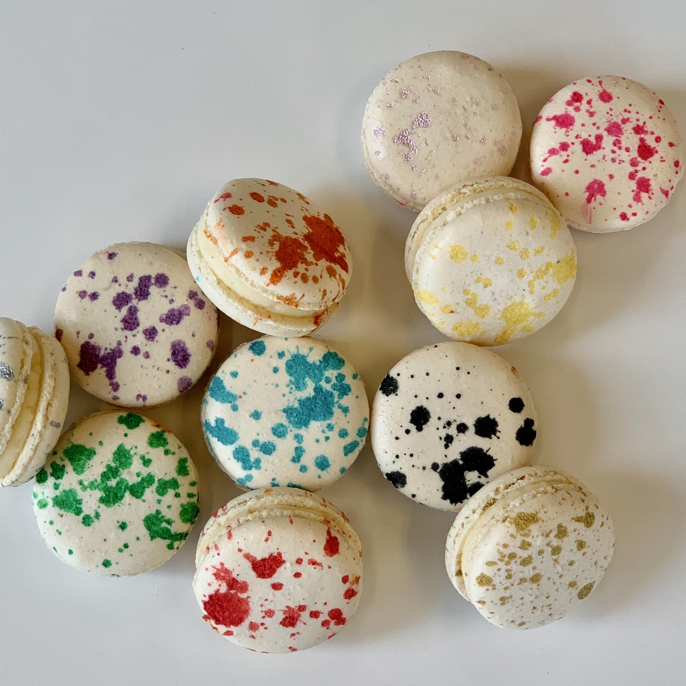Colorful macarons decorated with multicolored splatter patterns, arranged on a white surface.