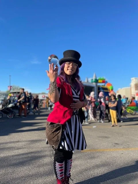 A woman dressed as a magician with a top hat holding a glass ball at a fairground.