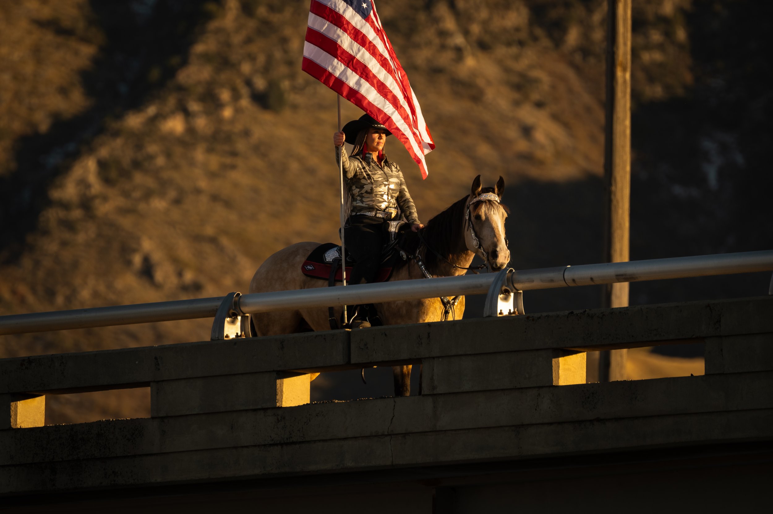 Women sitting on a horse on a bridge holding the american flag