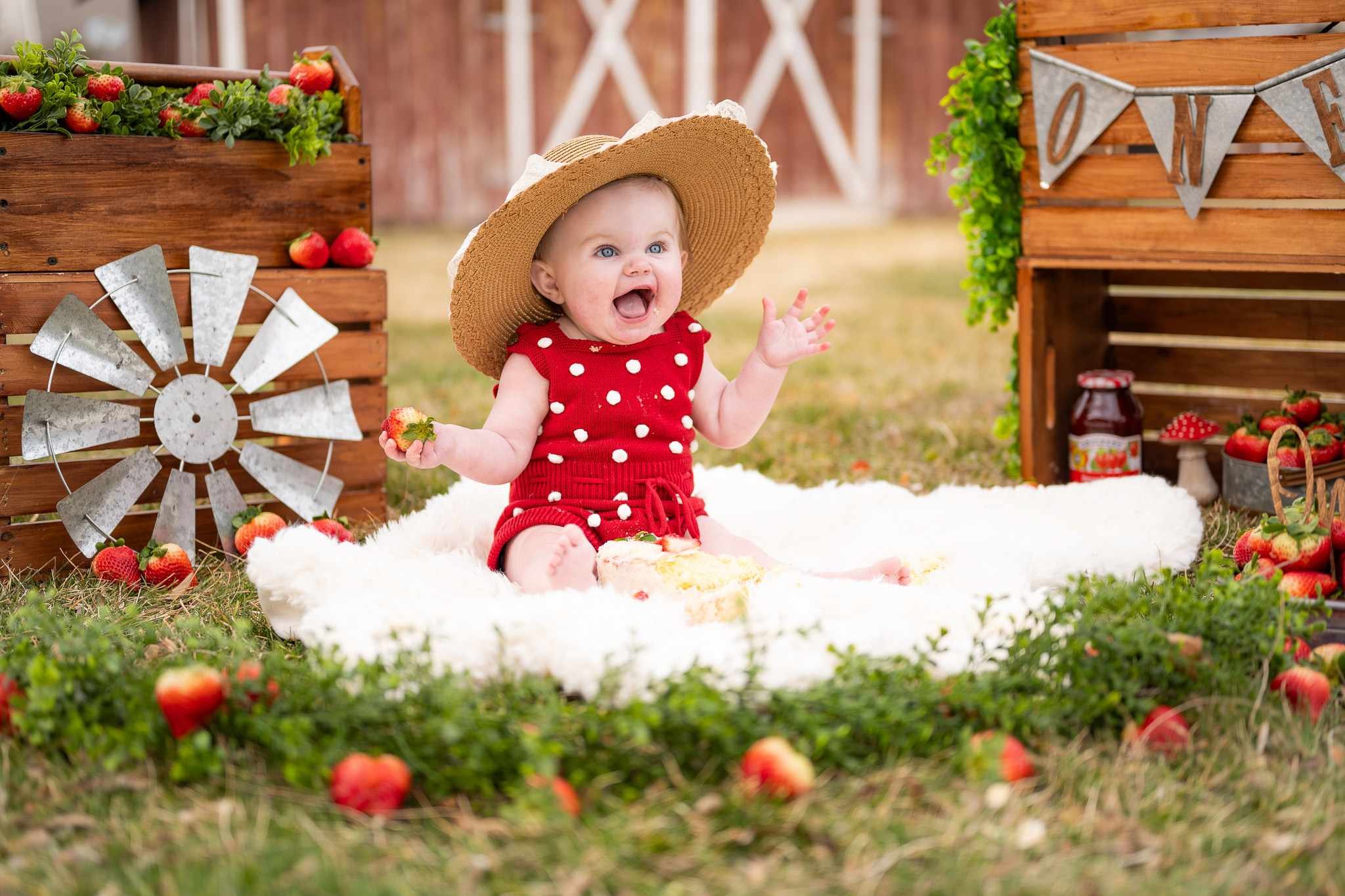A young baby wearing a hat and sitting on a rug with a "ONE" sign in the background